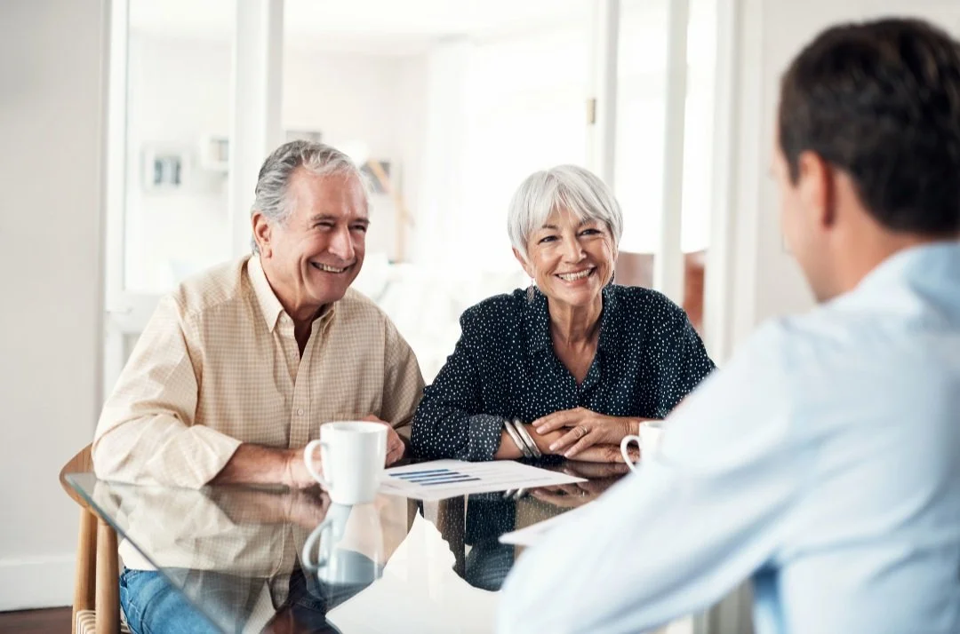 Smiling older couple meeting with a professional at a table with documents and coffee cups.