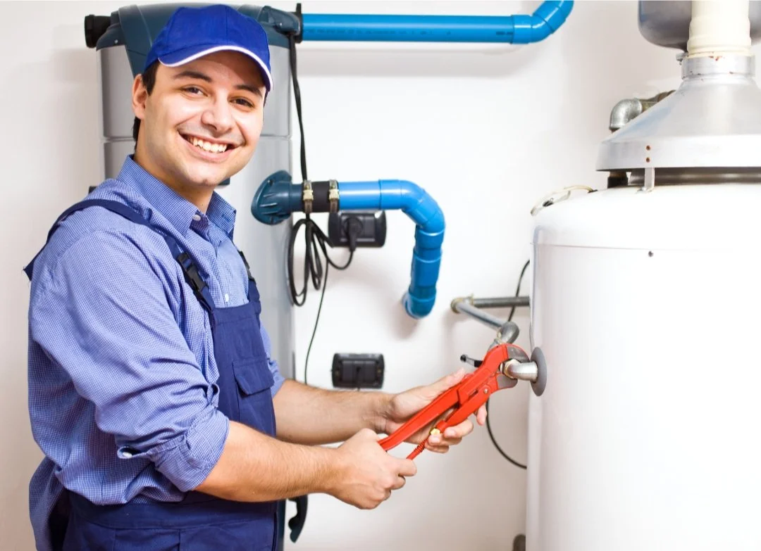 Plumber smiling while working on a water heater with a wrench.