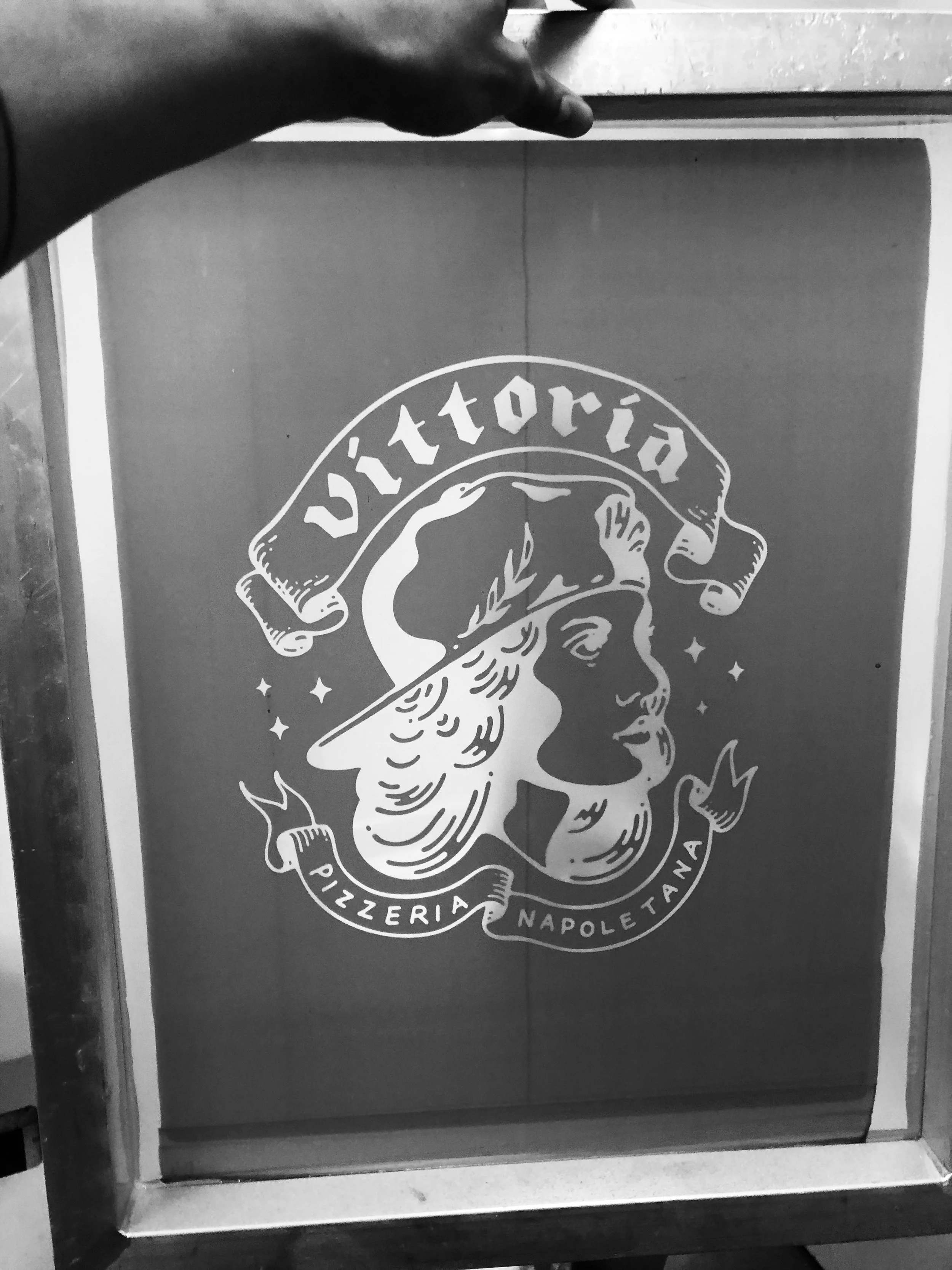 Black and white photo of a screen displaying the Victoría Pizzeria Napoletana logo with a woman wearing a bandana.