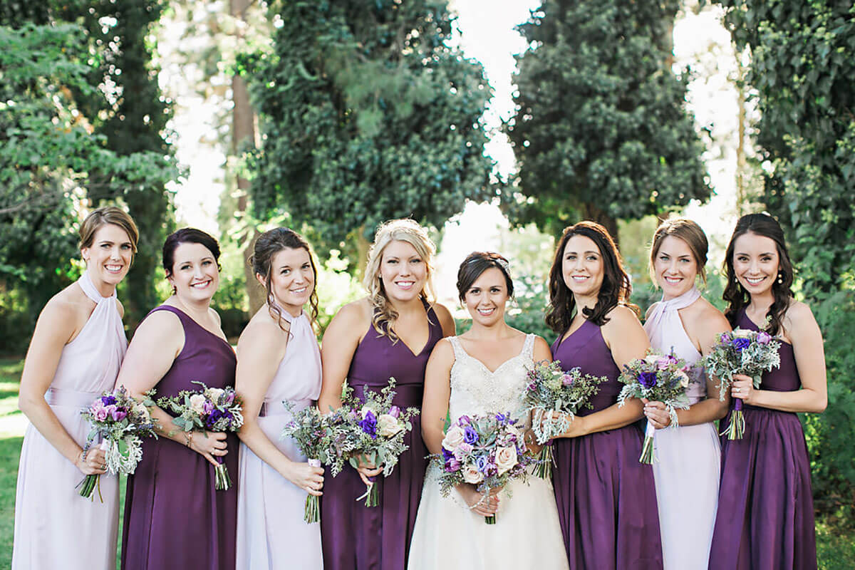A photo of a bride and her bridesmaids in white and purple with flowers