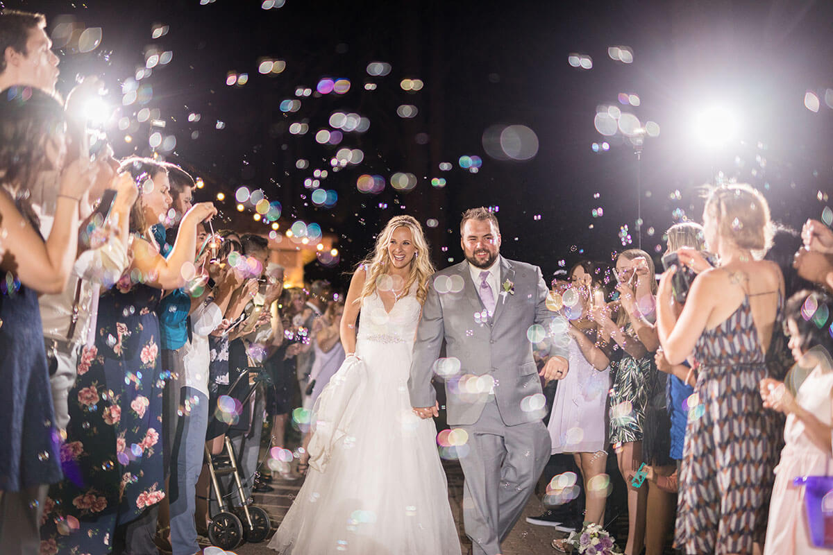 A photo of bride and groom surrounded by friends and family with lights and a dark sky