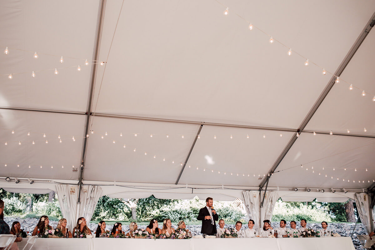 A photo of a man giving a speech at a wedding ceremony with lights hanging from the ceiling