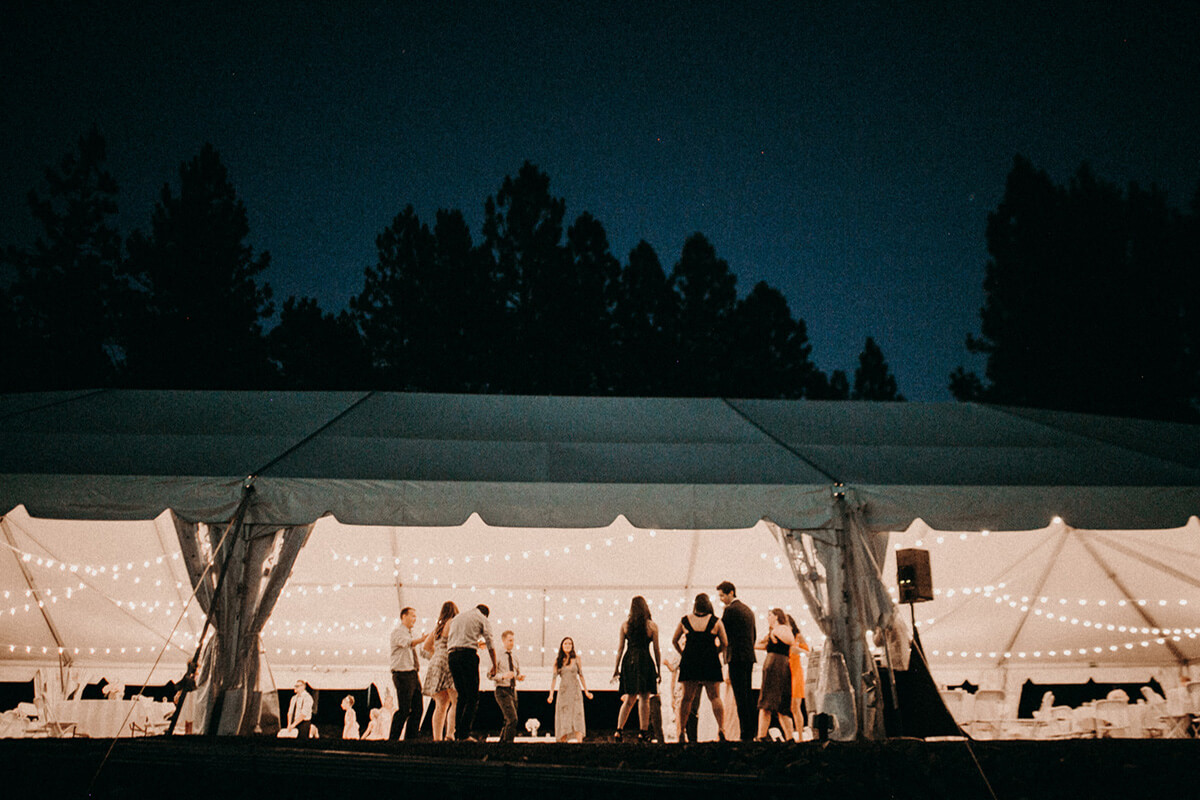 A night time shot of the wedding tent exterior with wedding party inside. Trees frame the photo against a night sky.