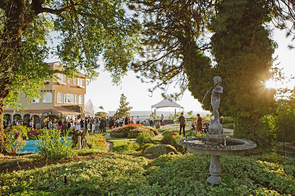 A sunlit photo of the Cliff House Estate and its surrounding courtyards. A crowd is gathered at the base of the Estate. 