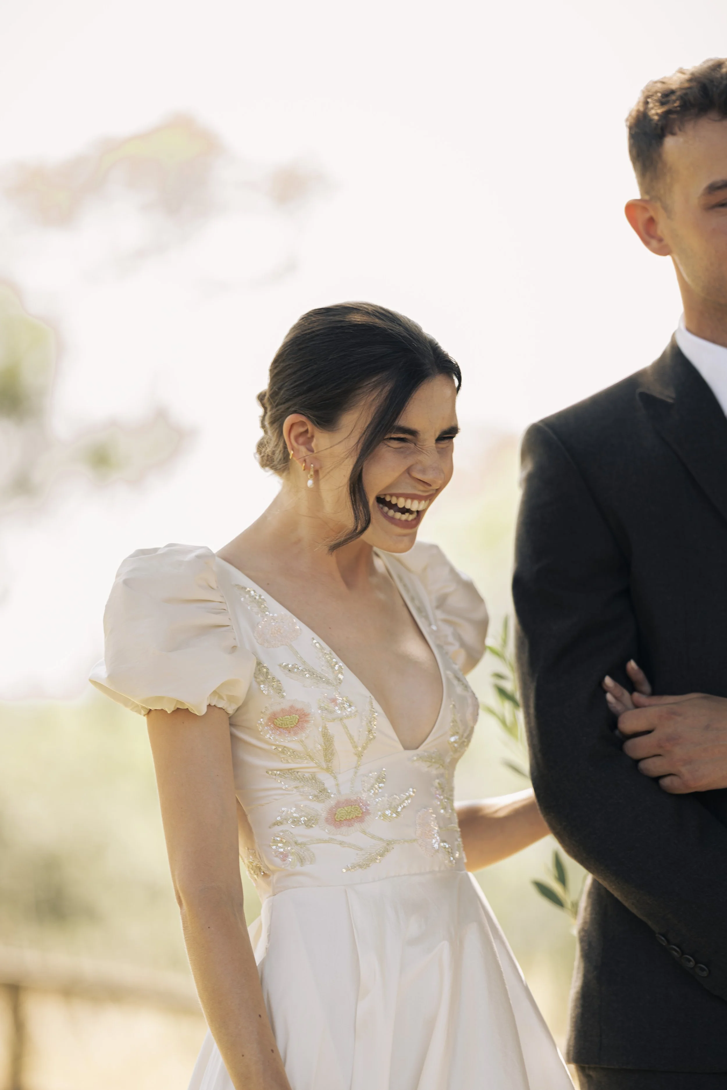 A woman in a white dress laughing with a man in a suit during a wedding ceremony outdoors.