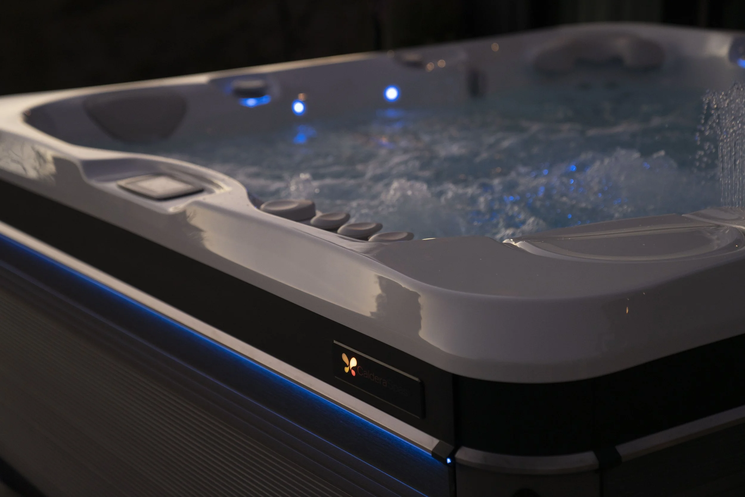 Close-up of a hot tub with blue LED lights and water bubbling, with control buttons visible at the side.