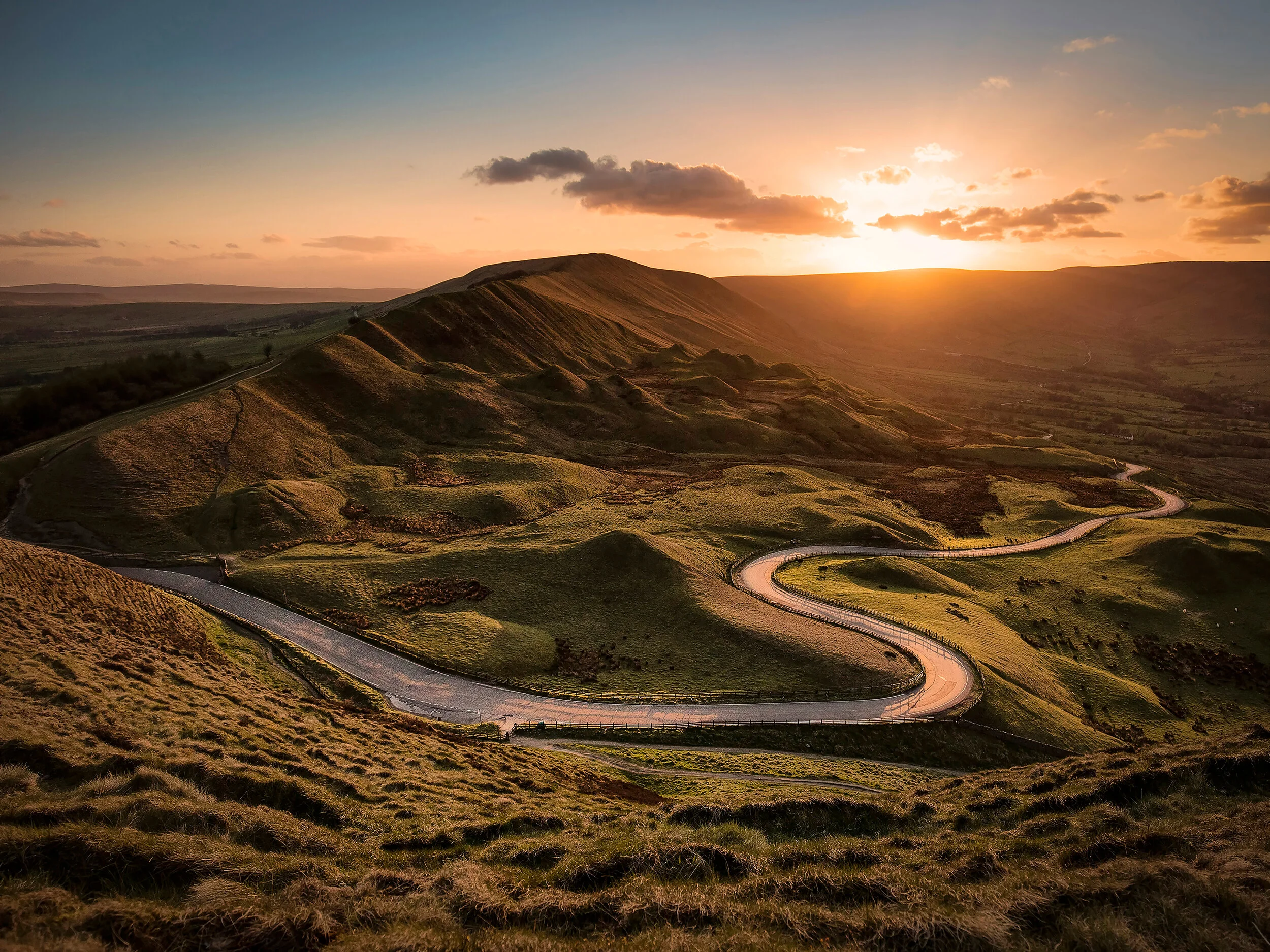 Scenic view of rolling green hills during sunset with a winding road cutting through the landscape.
