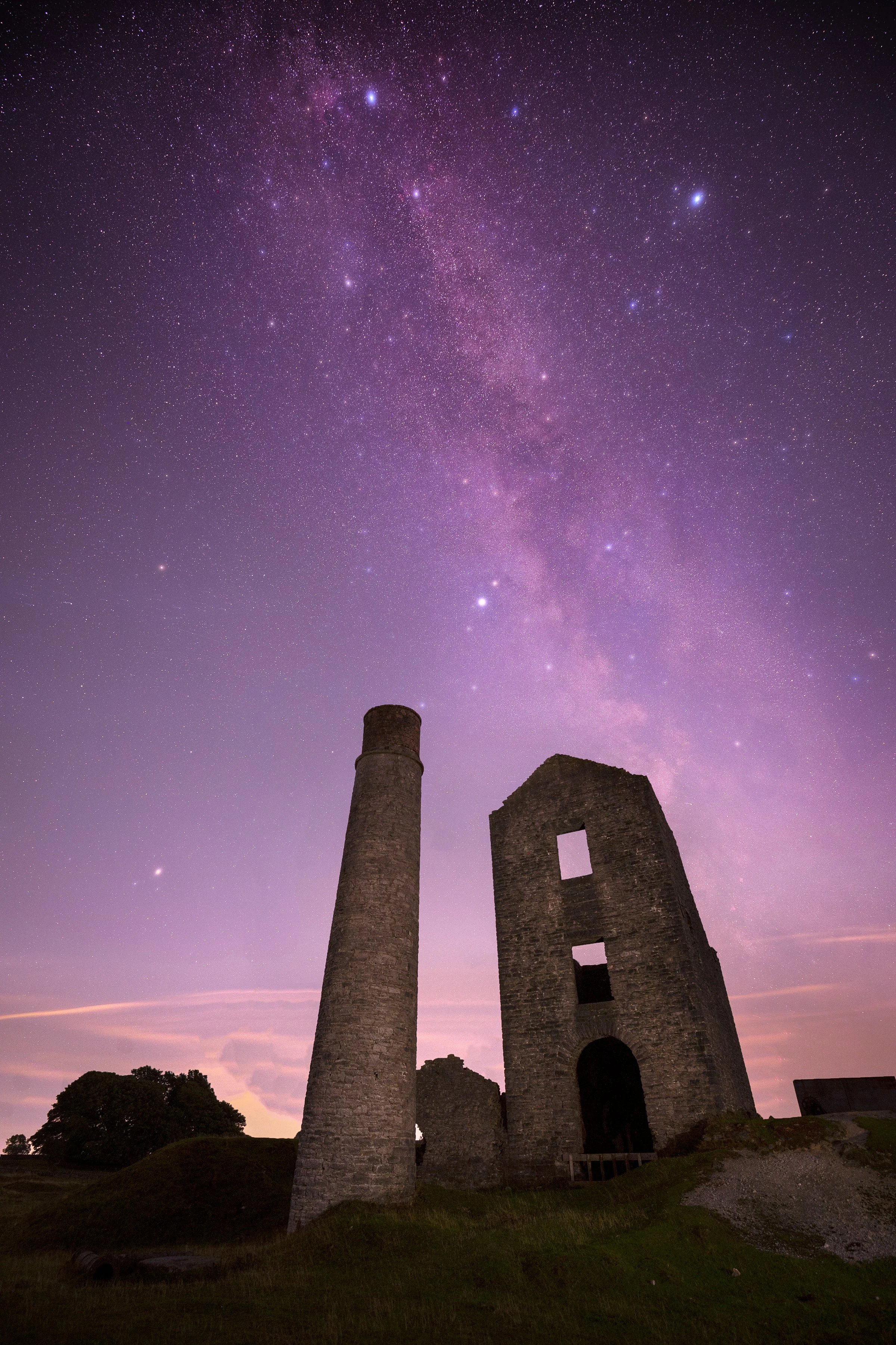 A night sky filled with stars and the Milky Way galaxy above ancient stone ruins and a chimney.