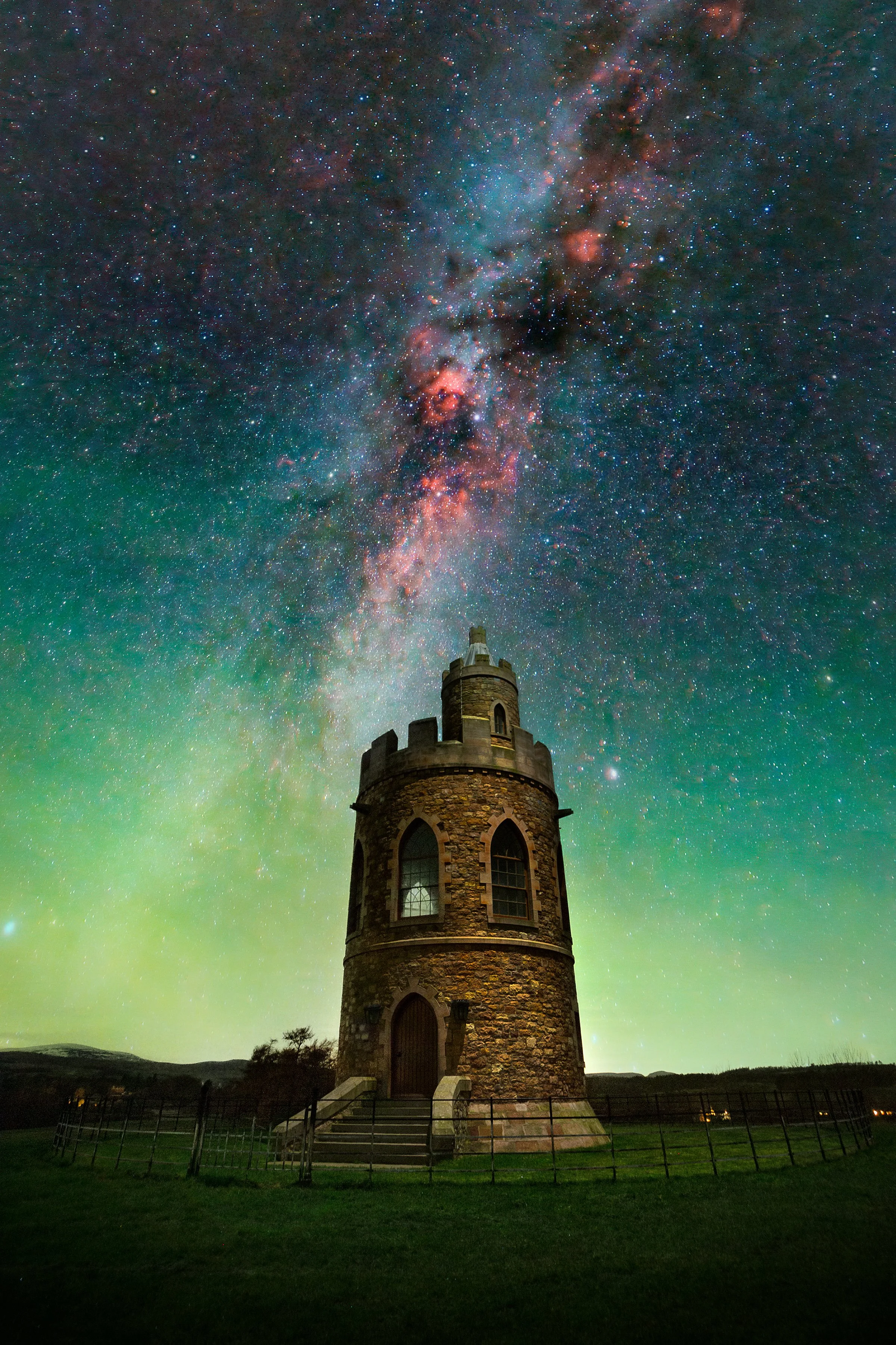 A stone tower sitting on grass with a star-filled sky and the Milky Way galaxy overhead at night.