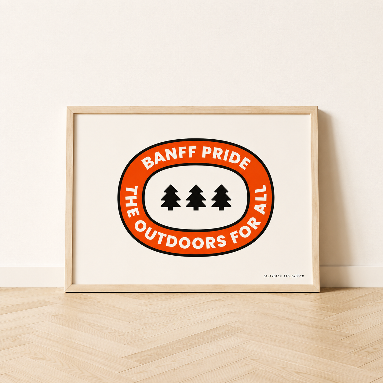 Outdoors For All art print in a natural wood frame, featuring a red oval badge with three black evergreen trees, white “Banff Pride” and “The Outdoors For All” text, and Banff coordinates.