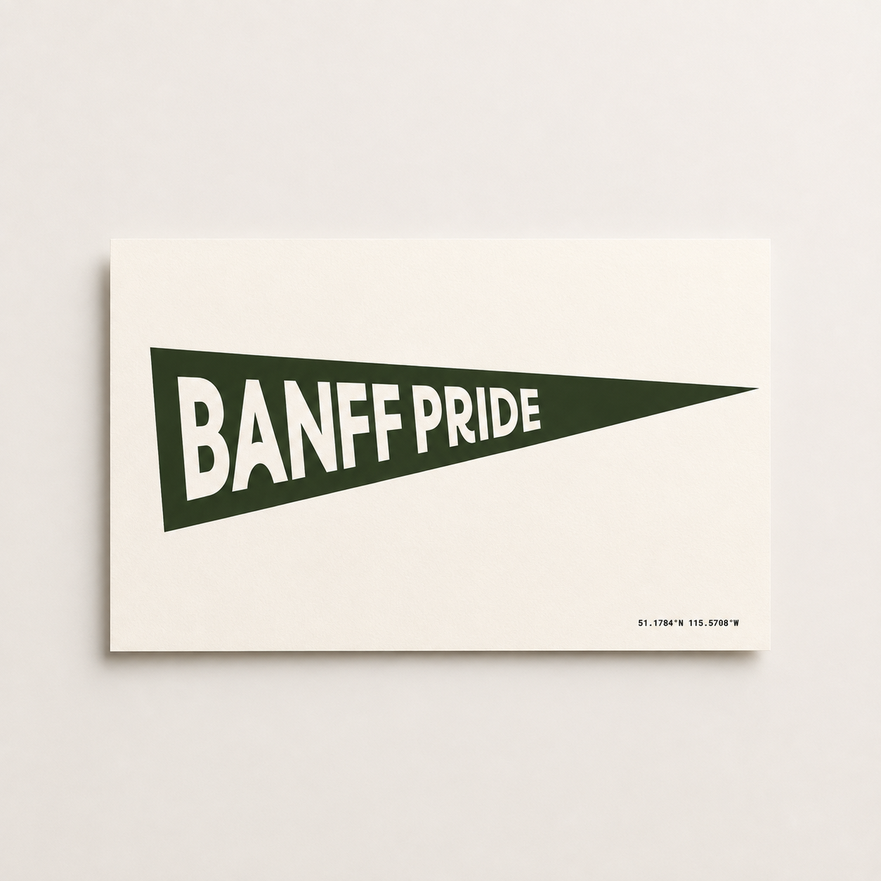 Banff Pride Pennant Flag art print featuring a dark spruce green triangular pennant with bold white “Banff Pride” lettering and Banff coordinates on a cream background.