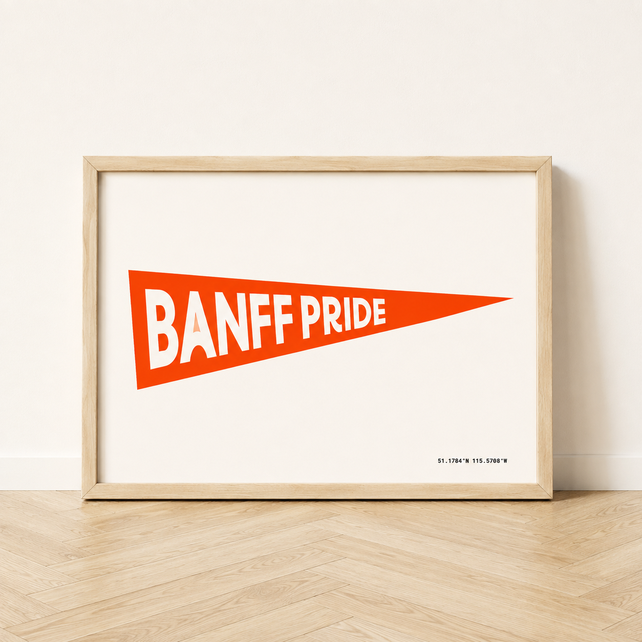Banff Pride Pennant Flag art print in a natural wood frame, featuring a bright fire red triangular pennant with white “Banff Pride” lettering and Banff coordinates on a cream background.