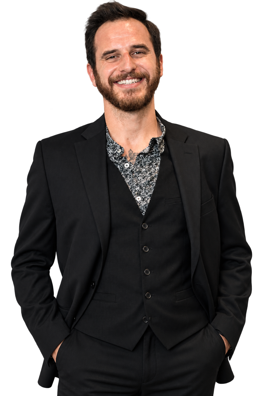 Russel Donahue with dark hair, beard, and mustache wearing a black suit jacket and a patterned shirt, standing against a black background.