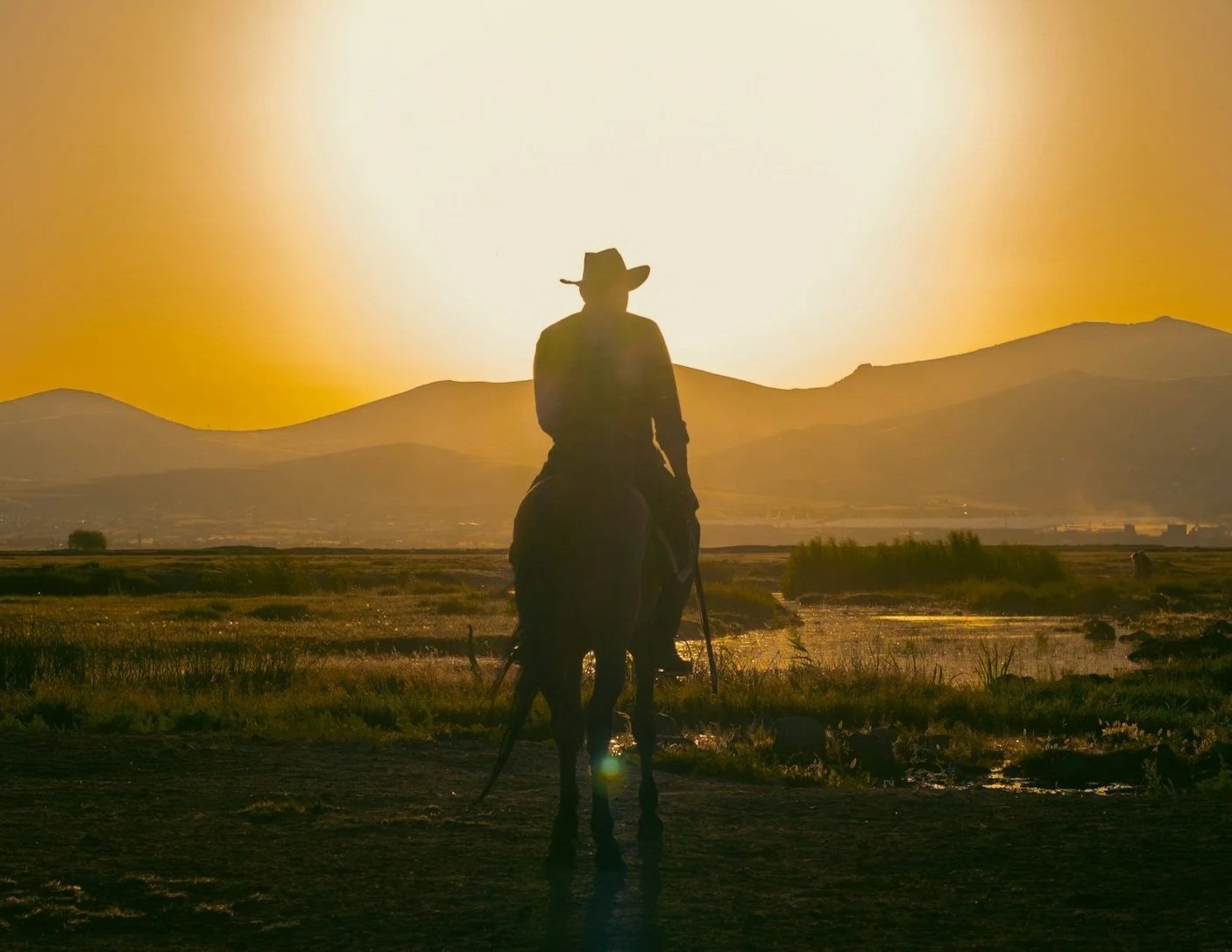 Photo of a cowboy on a horse riding towards the sunset
