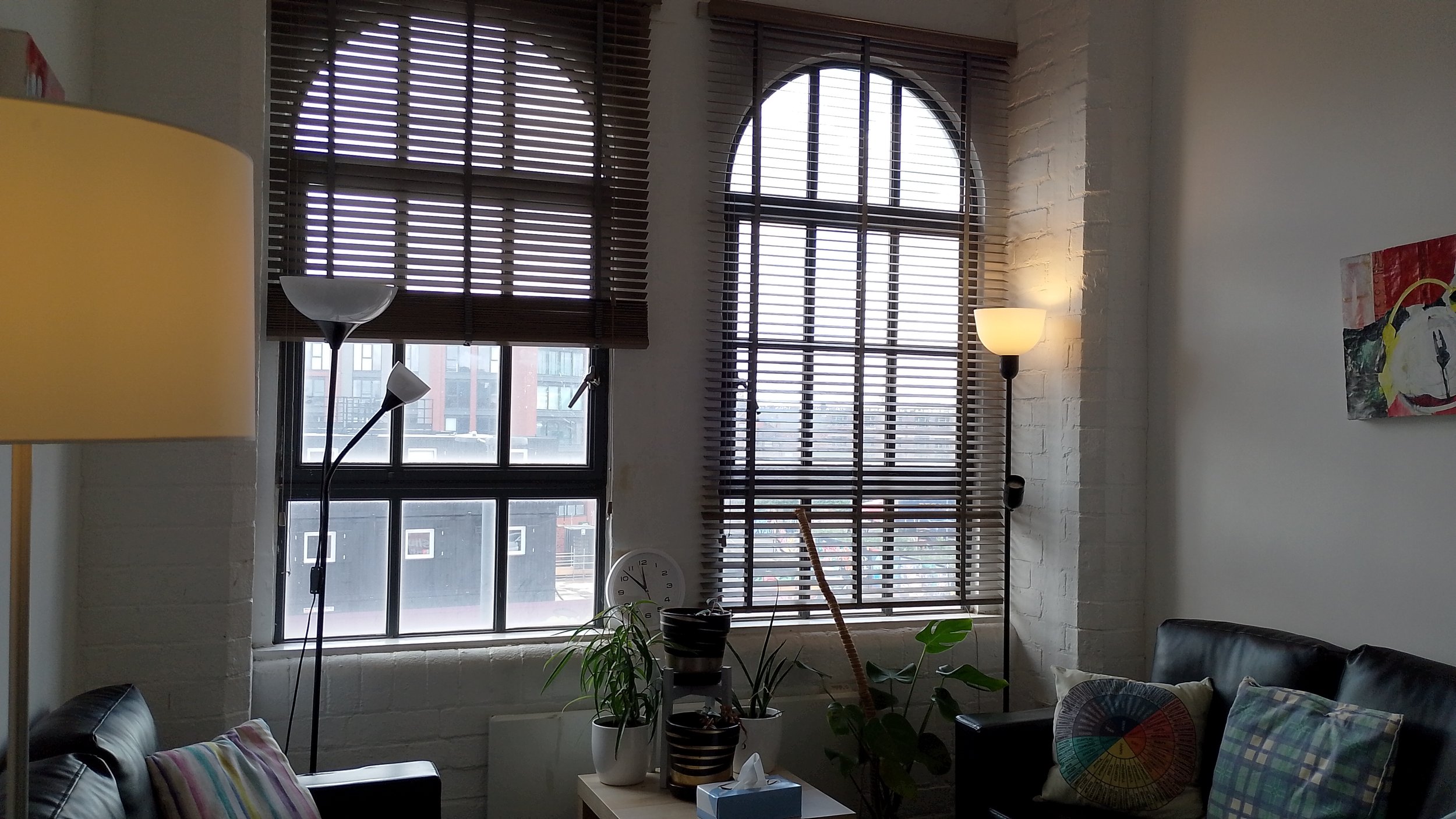Shaded office with 2 arched windows and black sofas.