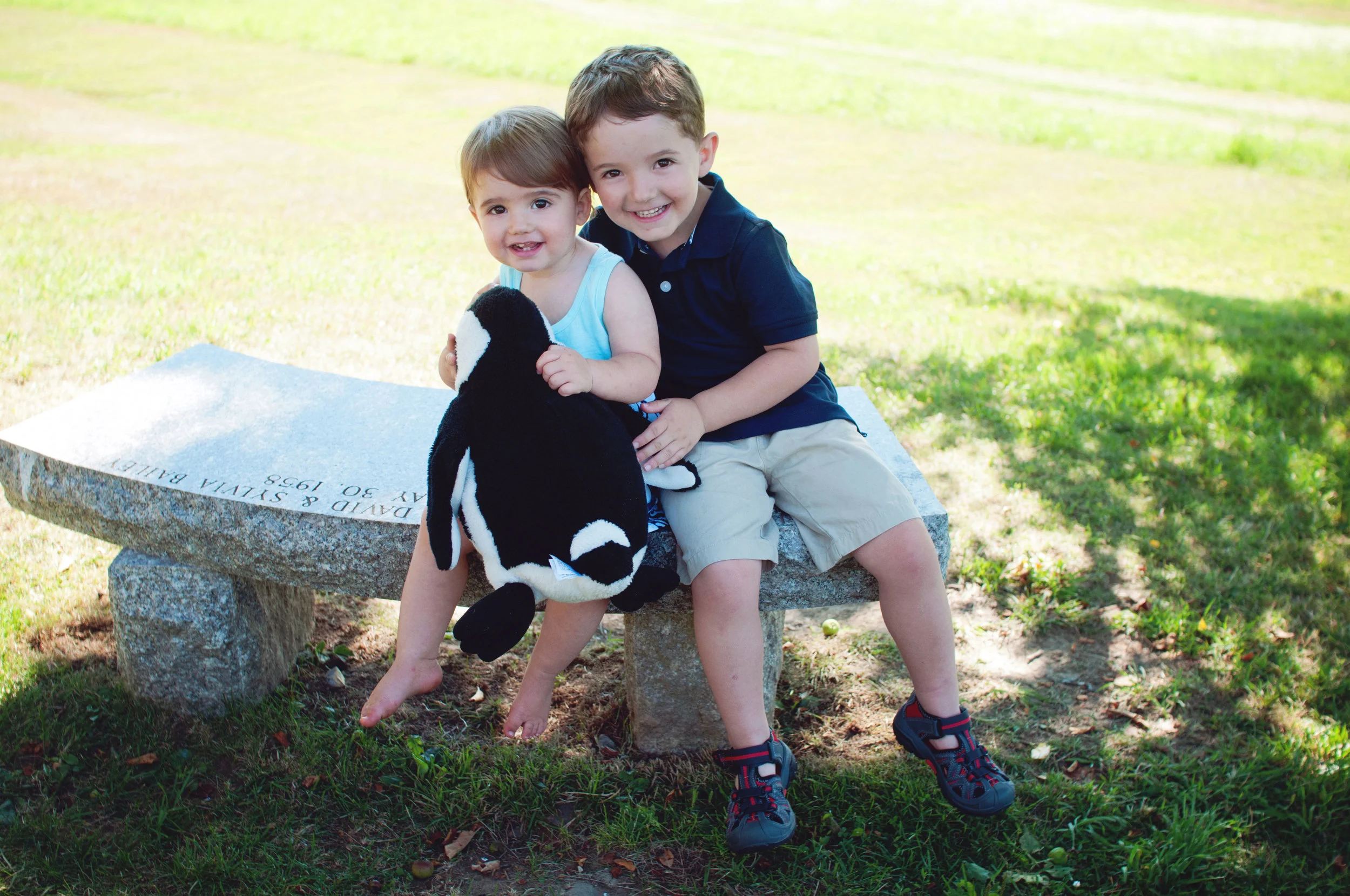 portrait of toddler and young boy sitting on a bench in the shade