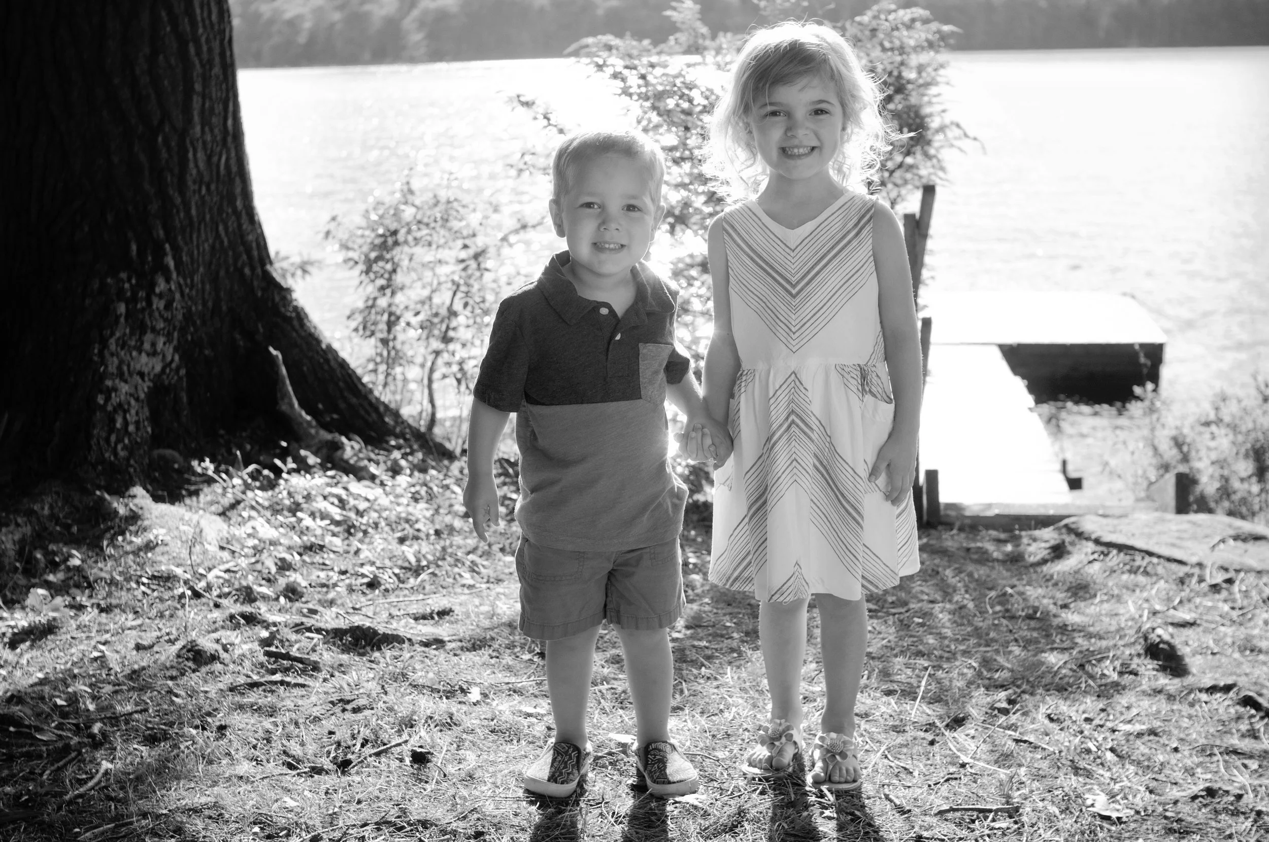 black and white photo of little boy and girl holding hands by a lake