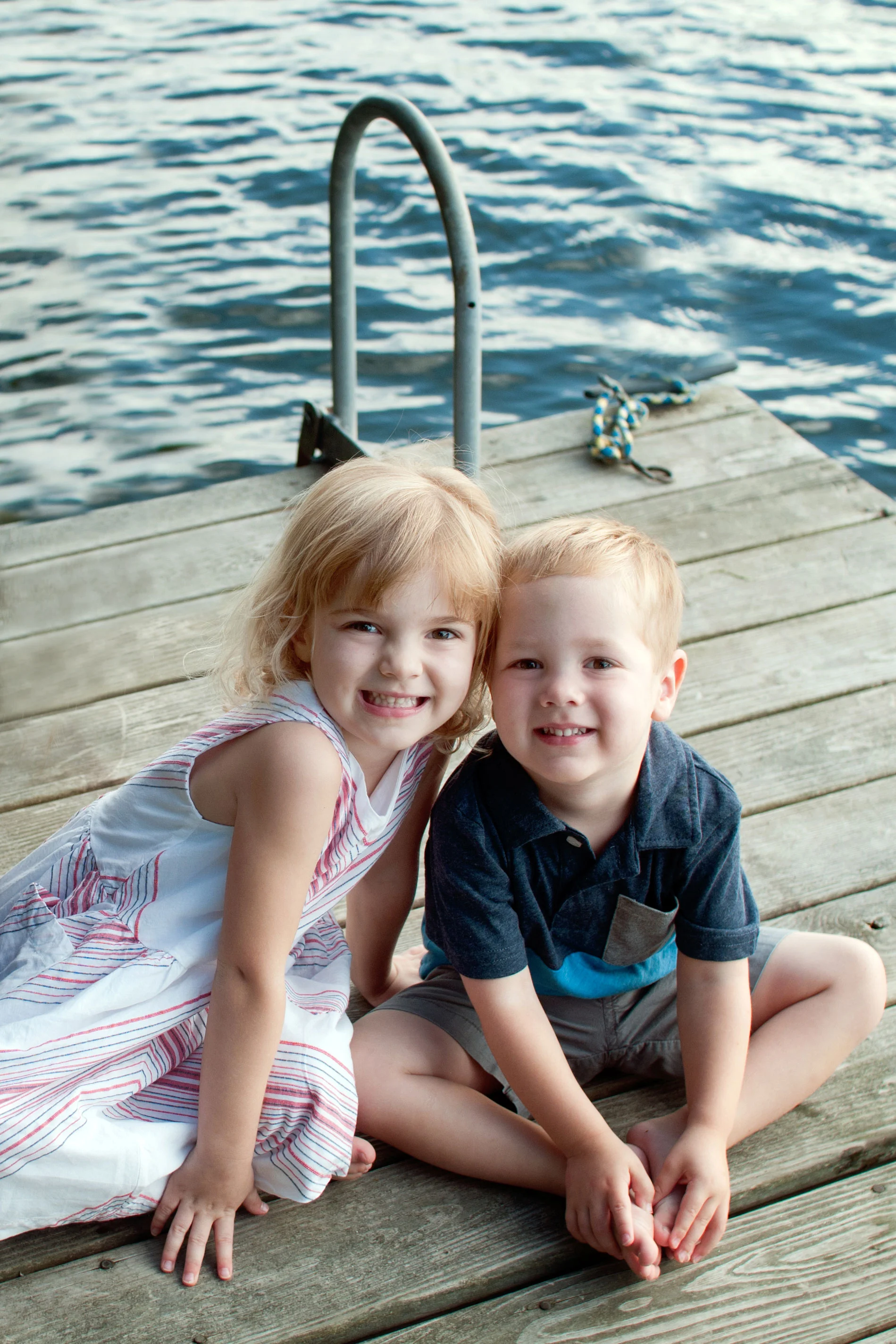 young girl and boy sitting together smiling on a dock