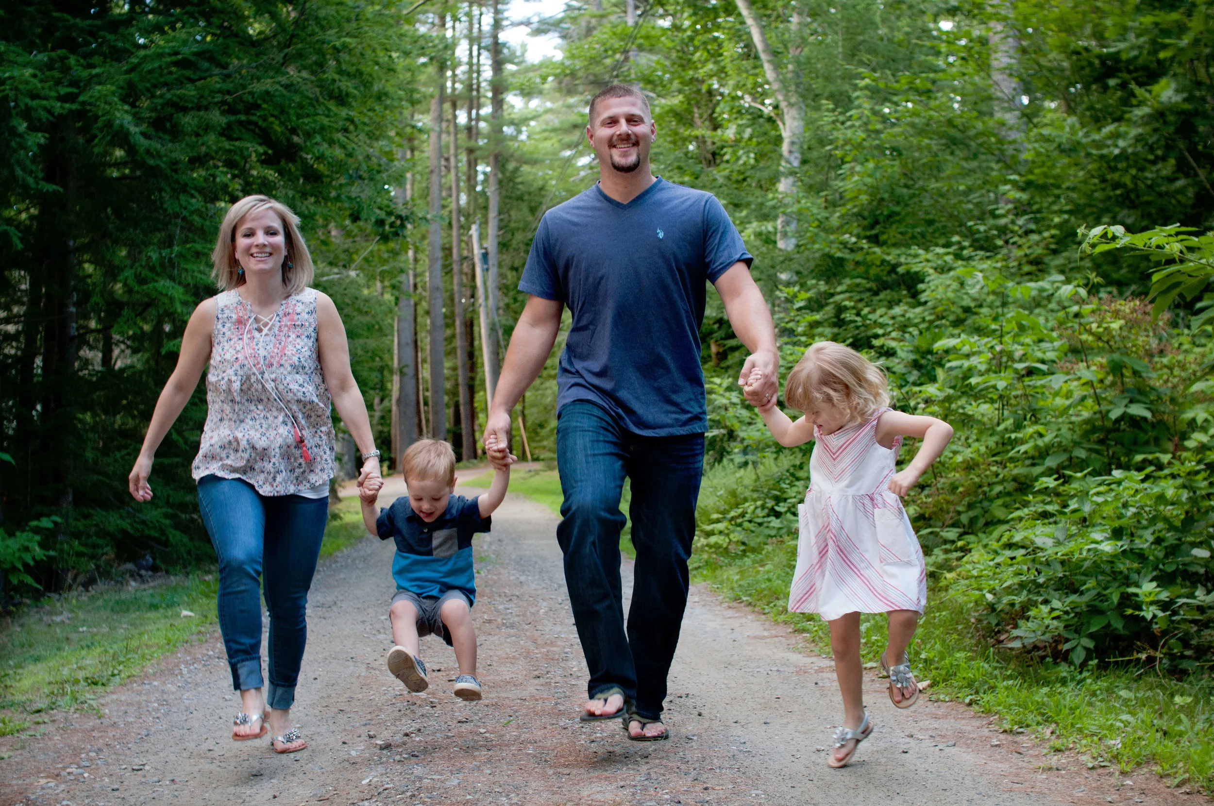 Family of four holding hands skipping on country dirt road