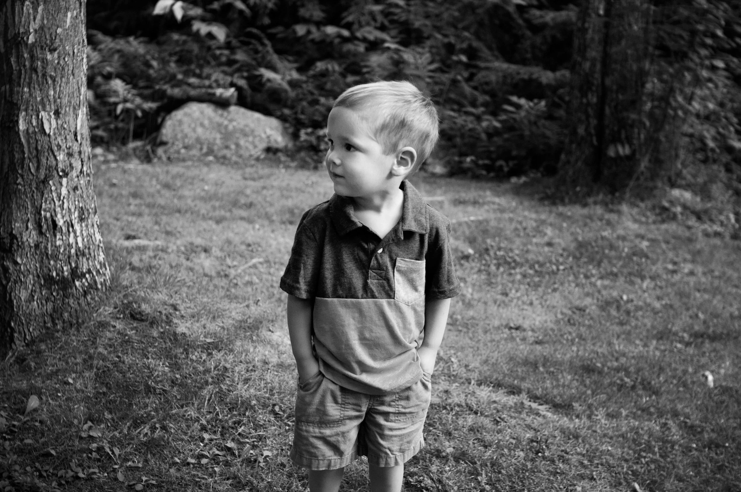 little boy standing in grass with hands in his pockets