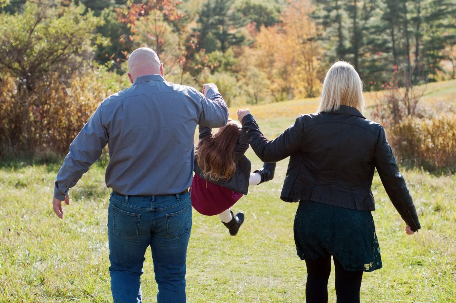 young family of three walking in a field in the fall