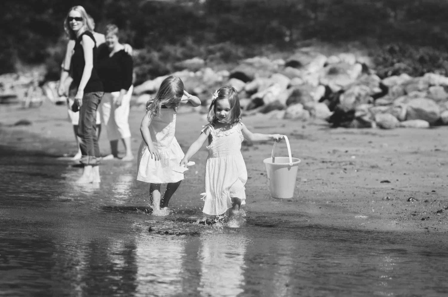 two little girls in white dresses running barefoot along the waters edge holding buckets
