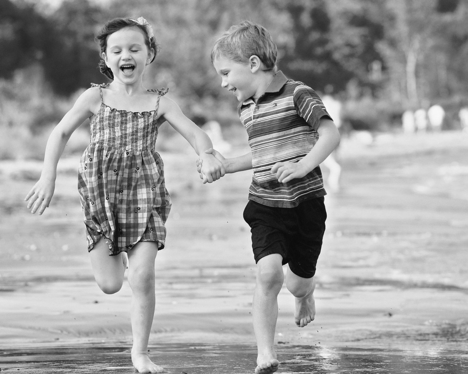 black and white photo of young twin boy and girl holing hands while running along the waters edge