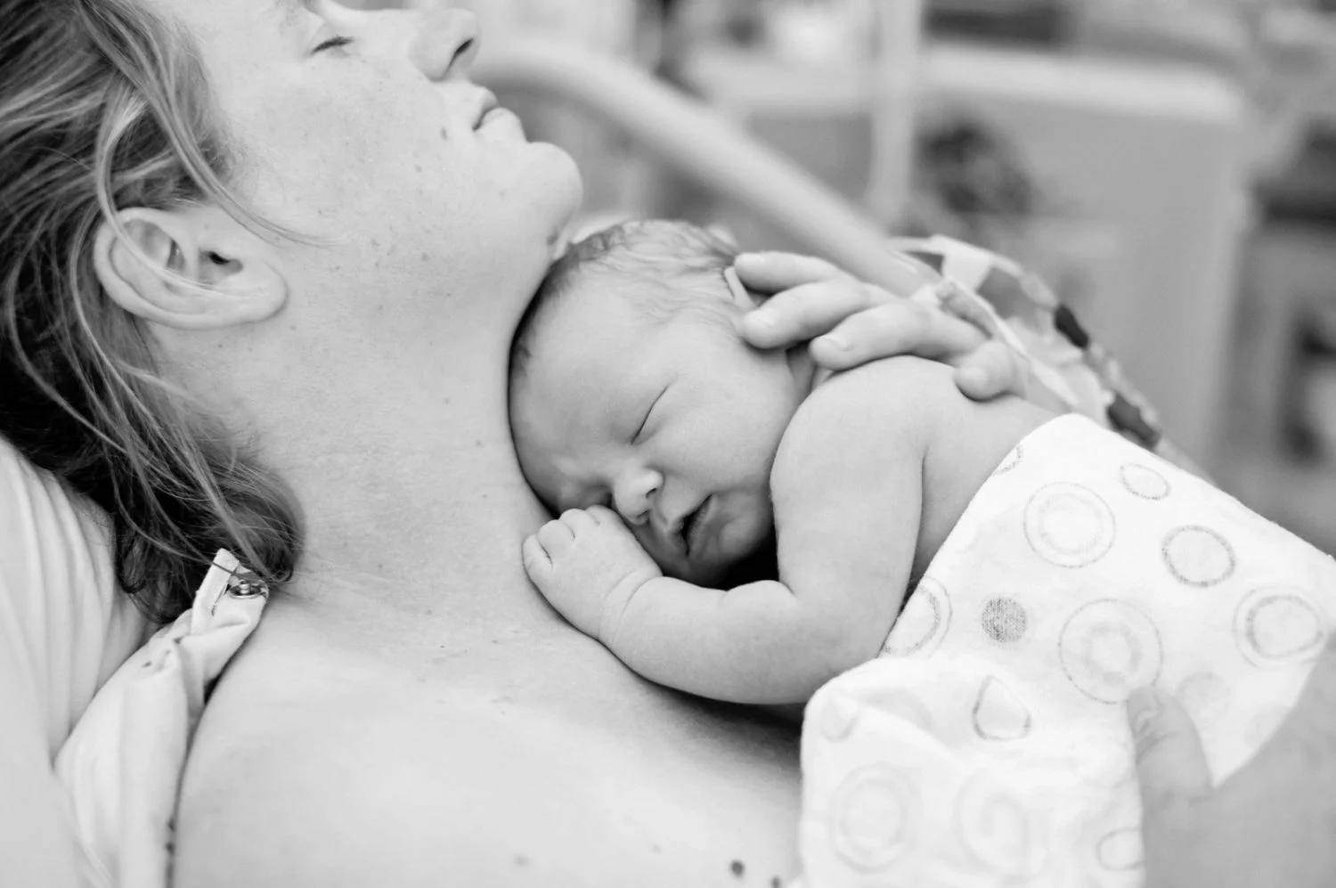 black and white image of mother sleeping with newborn on her chest