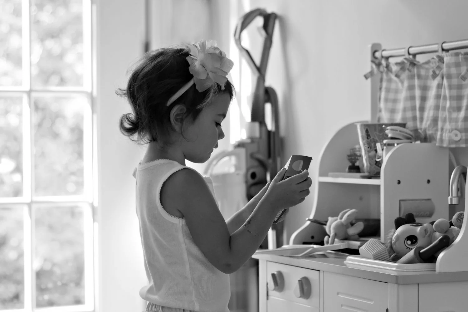 black and white photograph of little girl playing with toy kitchen