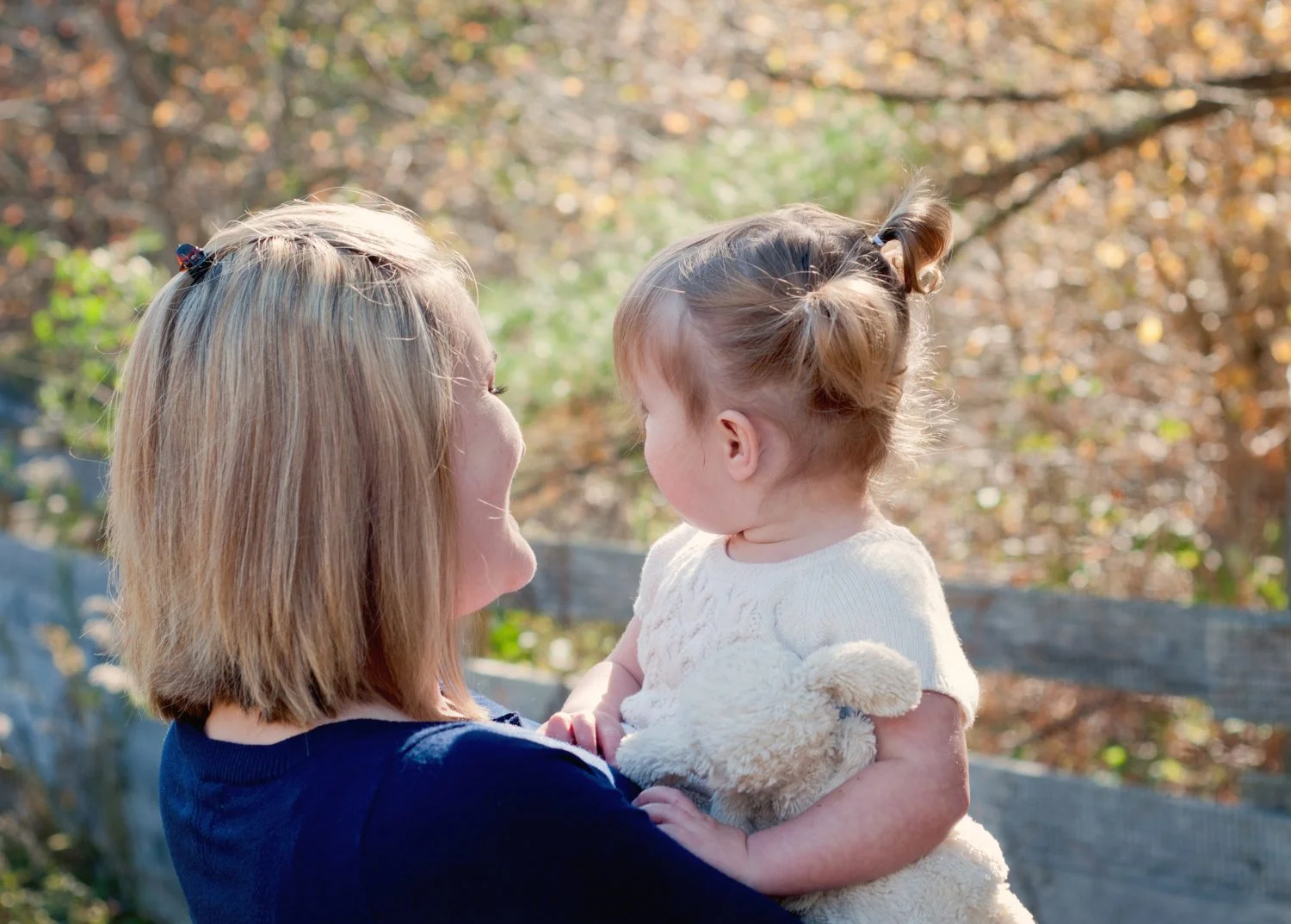 mother holding her toddler girl with sparkly fall colors in the background