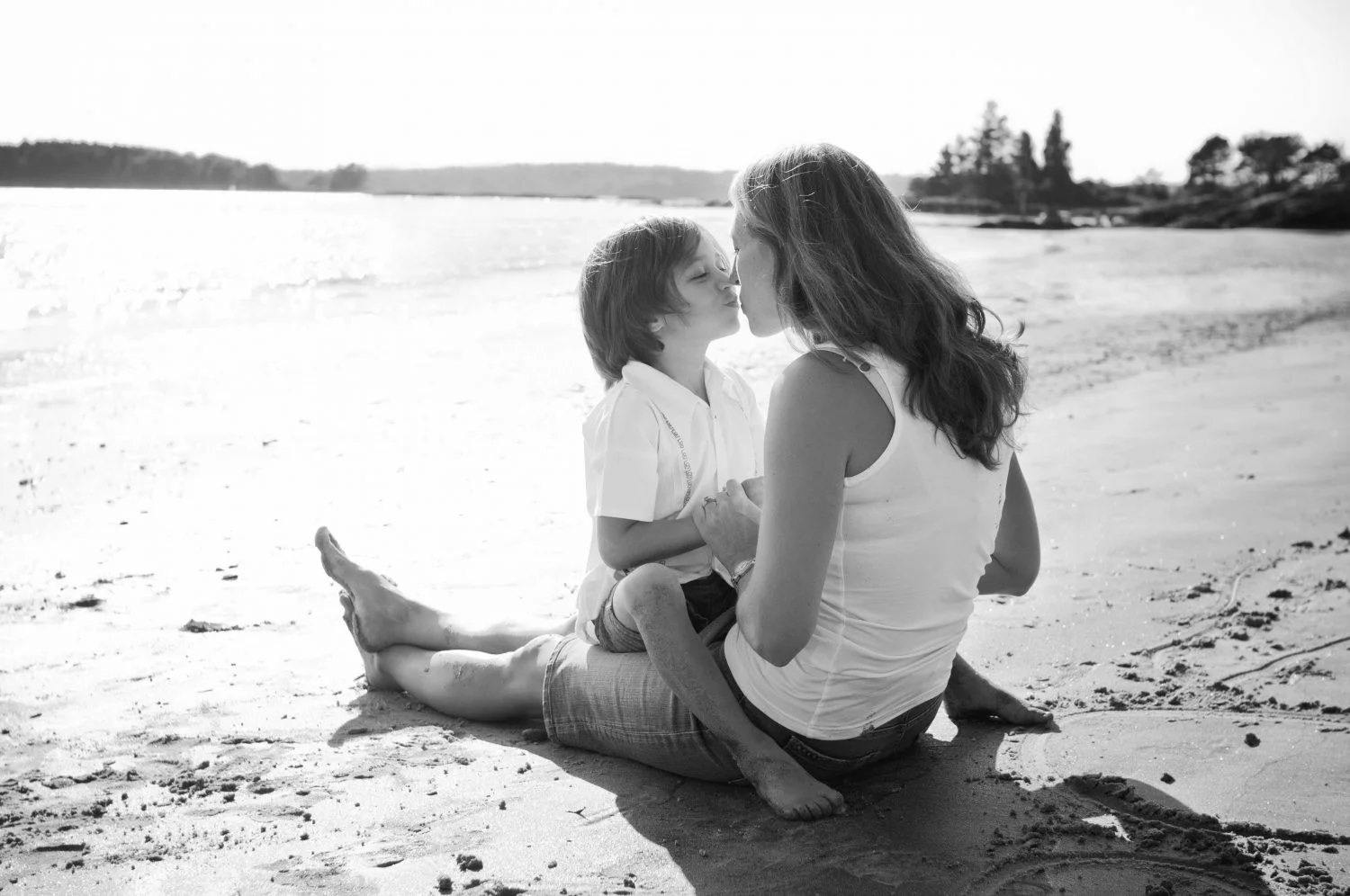 young son sitting on mothers lap facing her while on the beach