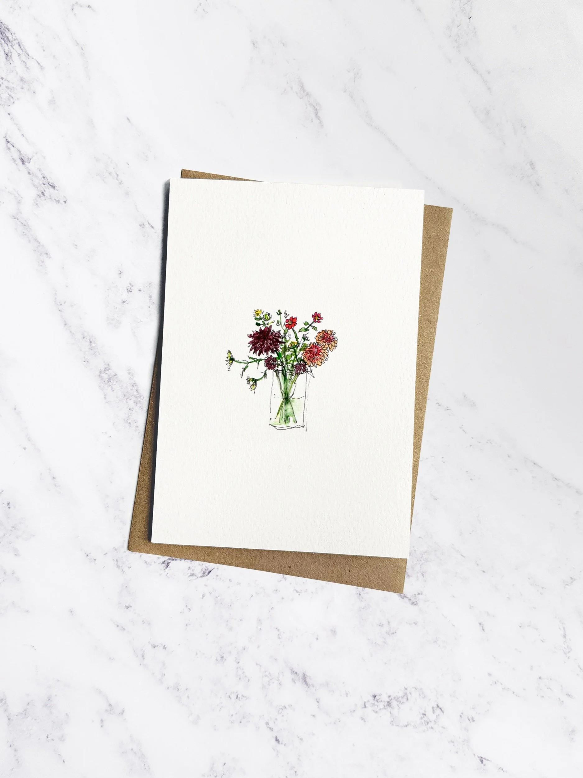 Beautifully hand painted watercolour illustration of autumn flowers & foliage in glass vase. The card is on a white textured paper with a brown kraft envelope behind sitting on a marble background.