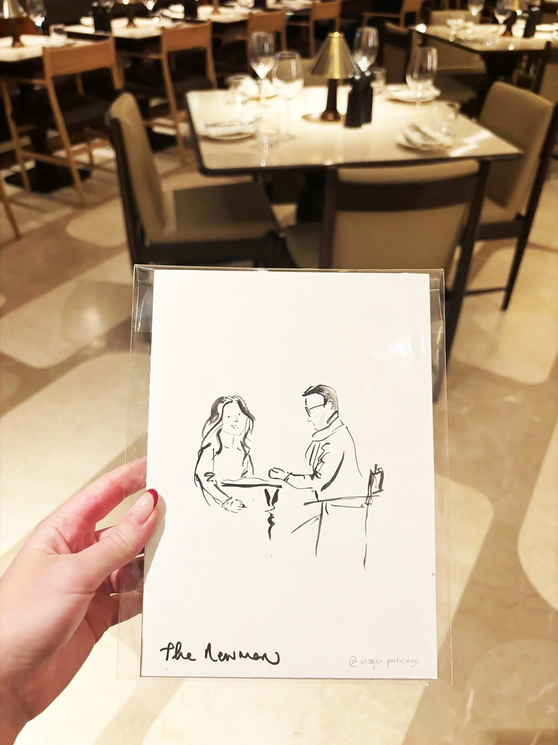 Hand holding monochrome watercolour illustration captured as a live illustration at The Newman London's restaurant opening. The restaurant can be seen in the background in soft focus