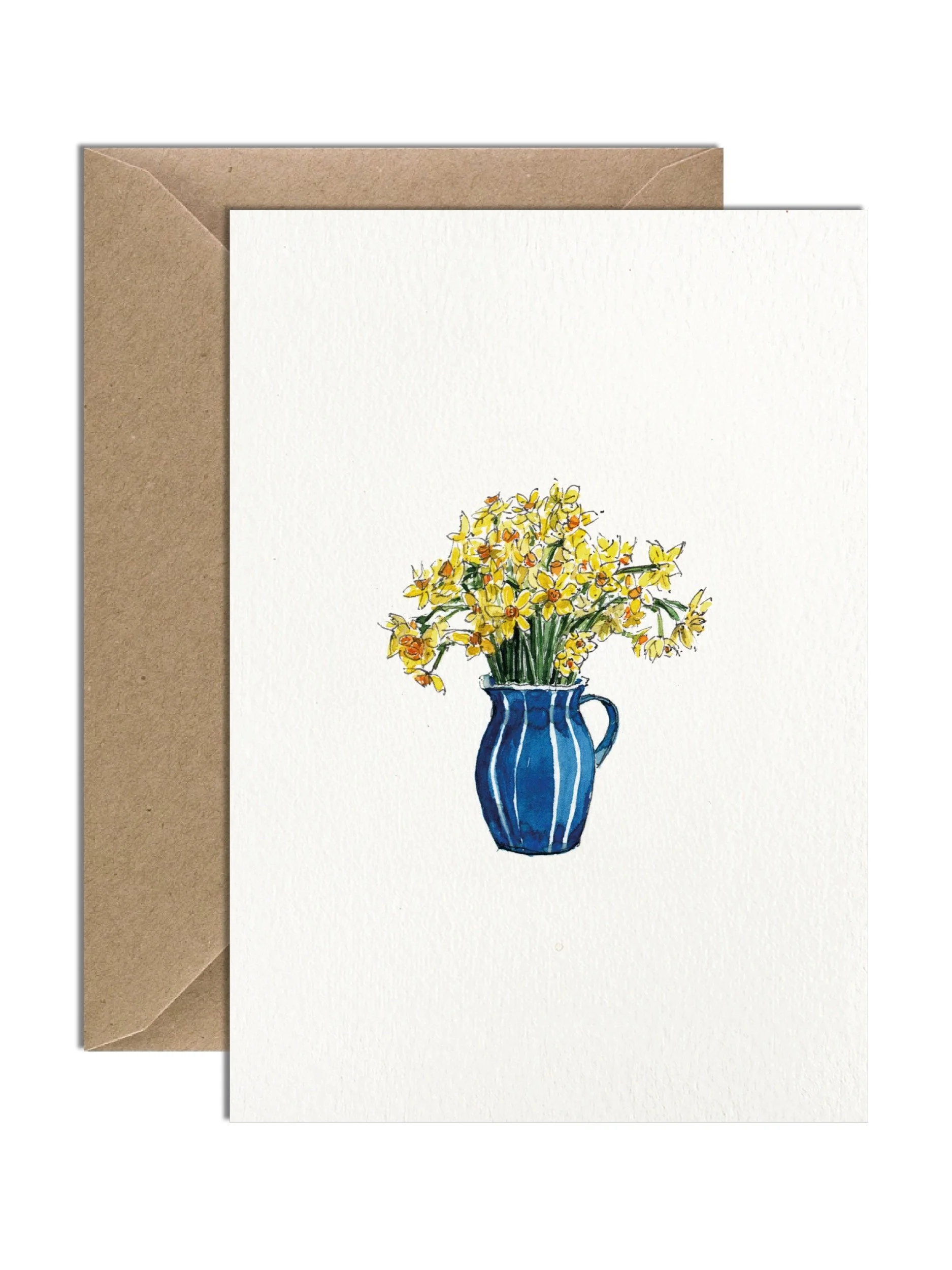 Bright yellow daffodil flowers sitting in a blue jug with little white stripes. The card is on an off white lightly textured card with a brown kraft envelope behind.