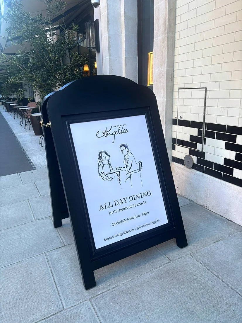 A board sign outside Brasserie Angelica, The Newman, London with live illustration couple portrait used as a central image to the sign.