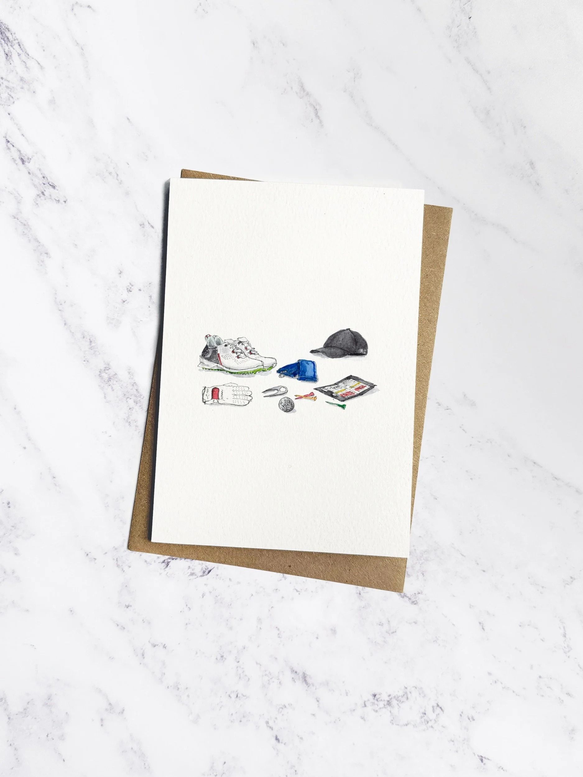 A beautifully illustrated golf-themed greetings card featuring a golf cap, gloves, and scorecard, displayed on a marble background with a kraft envelope.