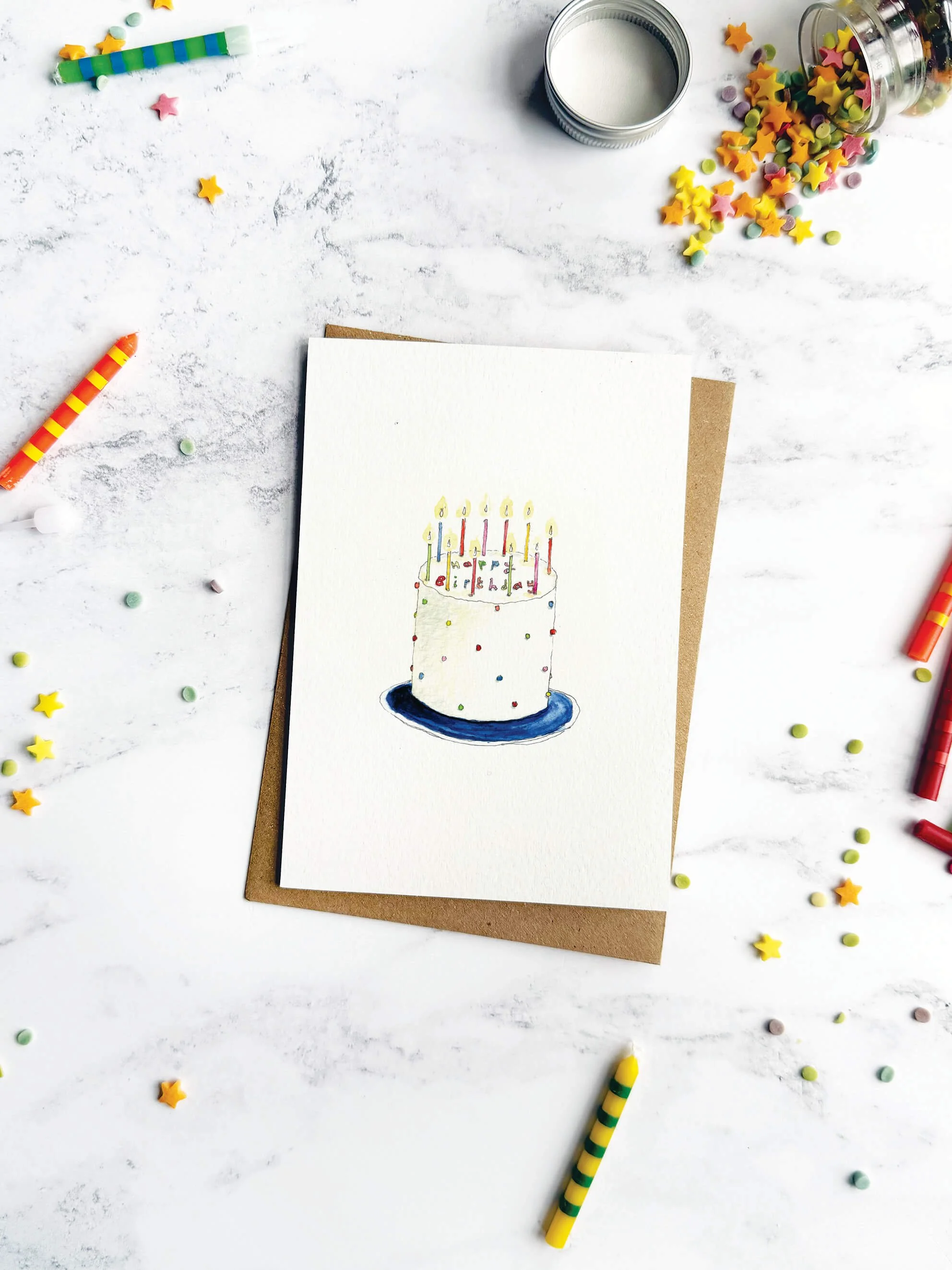 A whimsical birthday card featuring a simple yet joyful cake, styled with colourful, stripy candles and sprinkles on a marble backdrop.