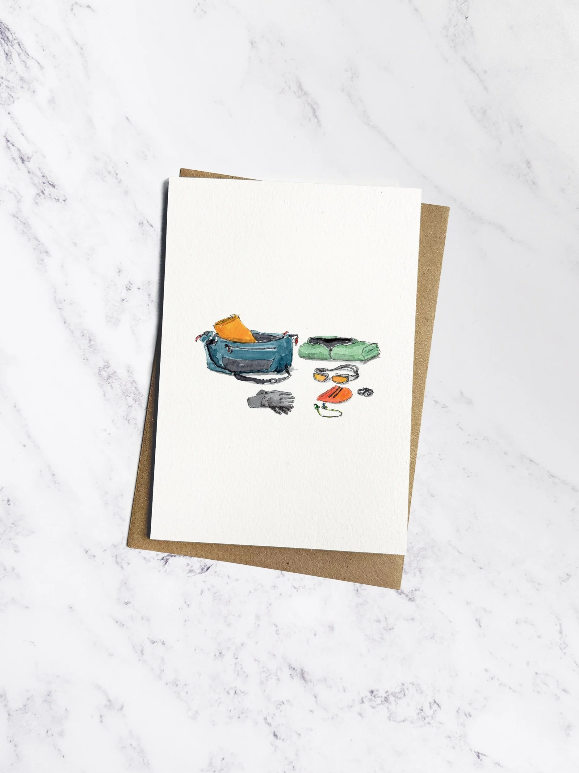 A beautifully illustrated swimming-themed greetings card featuring a dry robe, swim hat, goggles, and earplugs, displayed on a marble background with a kraft envelope.