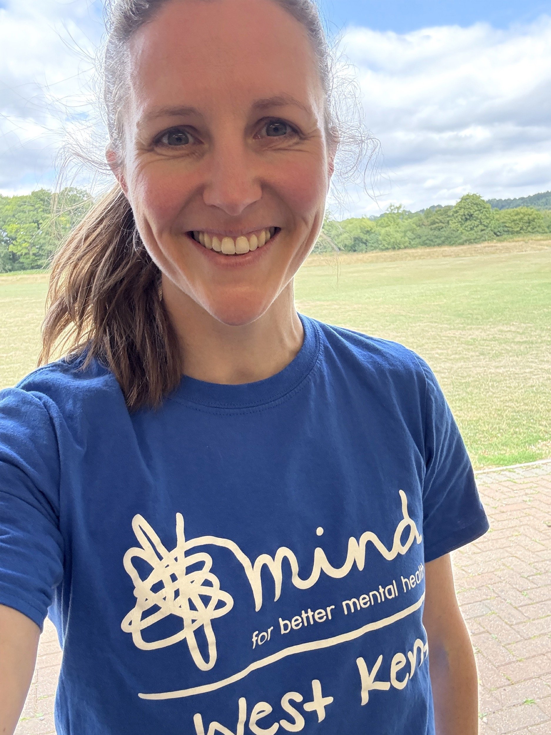 Imogen Partridge a white thirty something year old female smiling at the camera wearing a blue West Kent Mind tshirt