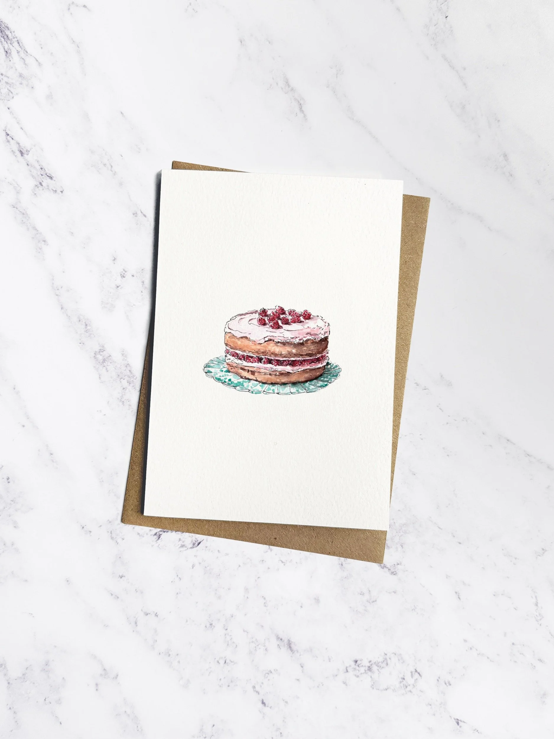 An elegant illustrated birthday card featuring a raspberry & marzipan cake with soft pink icing, fresh raspberries, on a scalloped ceramic plate. With a kraft envelope on a white marble background.