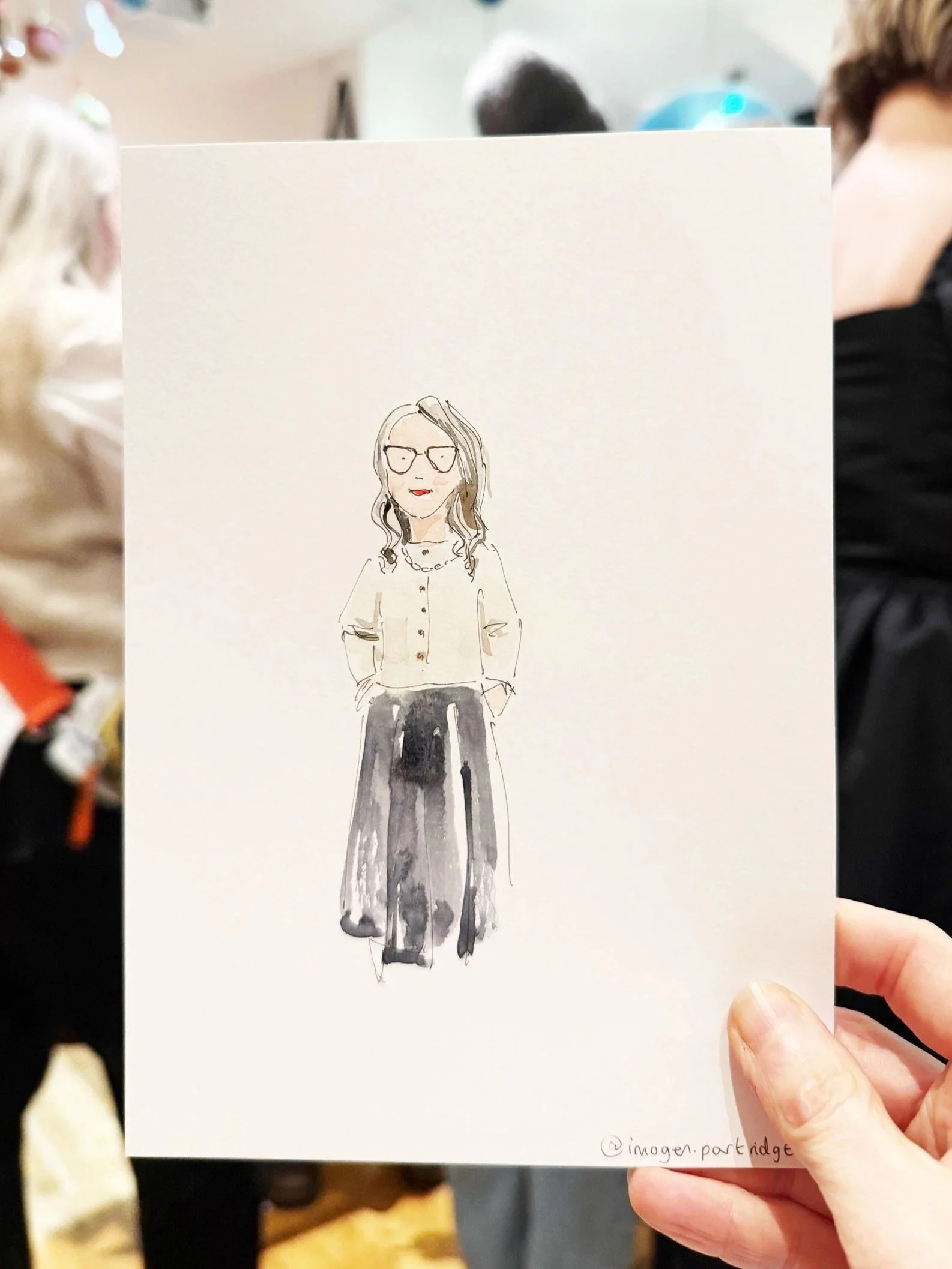 Loose watercolour live portrait illustration of a chic lady with grey hair, cream cardigan and dark skirt. Held up at an event in London for Penguin
