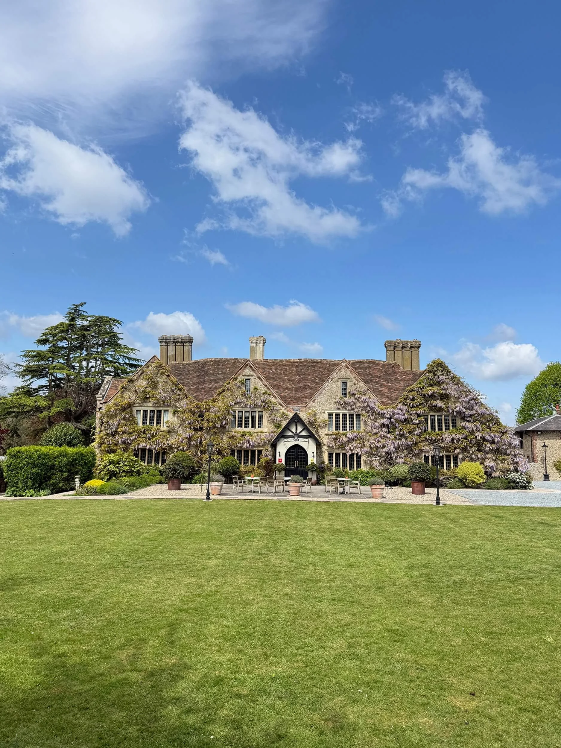 Boys Hall venue in Ashford Kent covered in wisteria, setting for a corporate watercolour workshop. The wisteria covered building is in the middle of the photo, with blue sky above and a lush green lawn in front.
