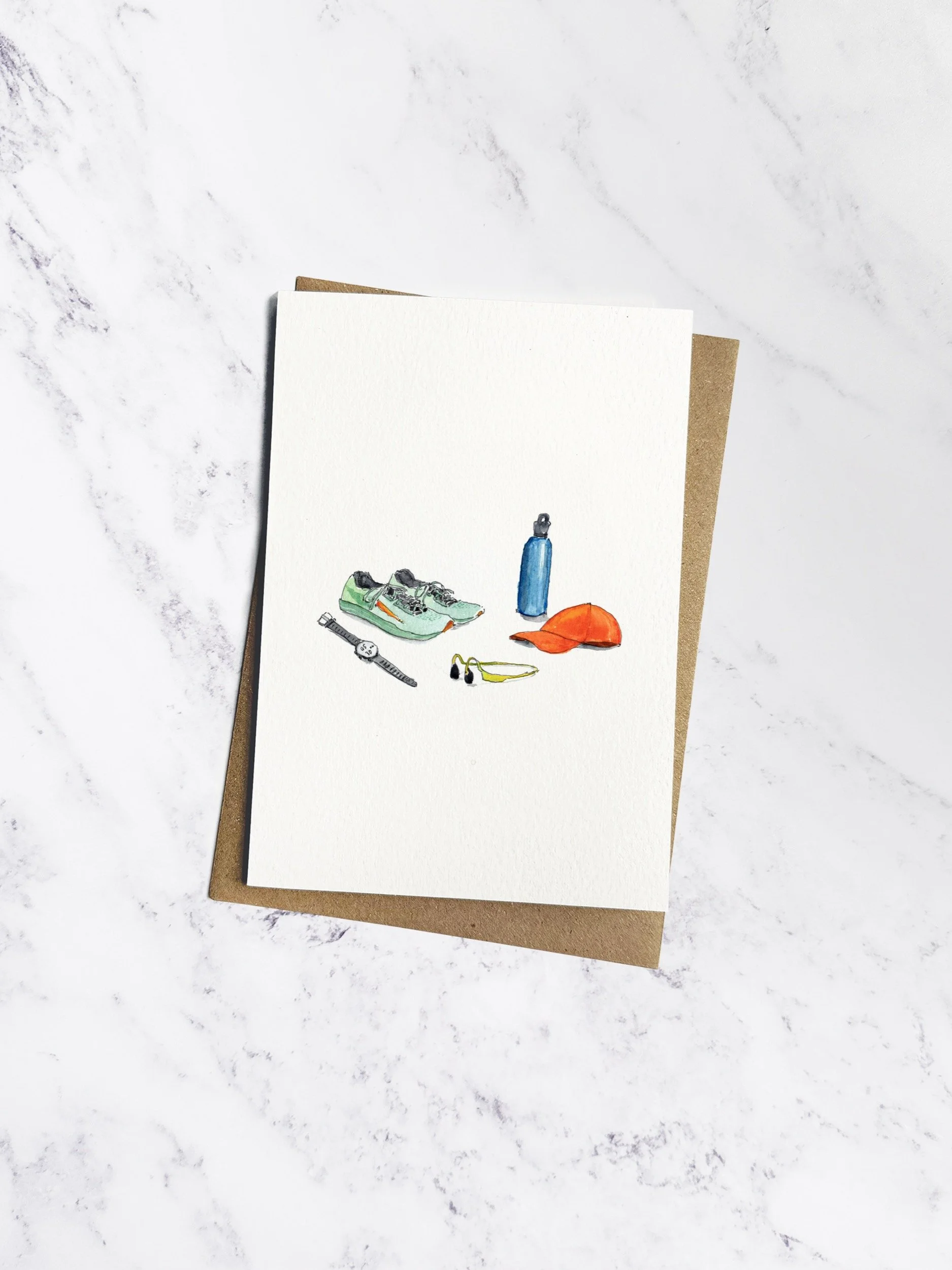 A running-themed greetings card featuring hand-painted watercolour illustrations of running shoes, a water bottle, and earphones, displayed on a marble background with a kraft envelope.