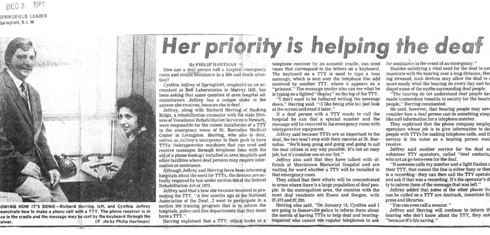 [Image description: a black and white newspaper clipping from 1981, where a man in a suit sits on a desk next to a woman demonstrating how to make a phone call with a TTY. Caption reads, Her Priority is helping the deaf.]
