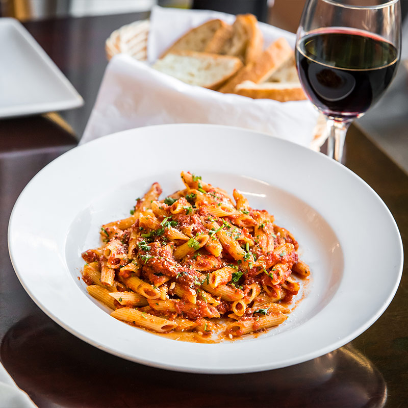 penne pasta dish with bread and glass of wine