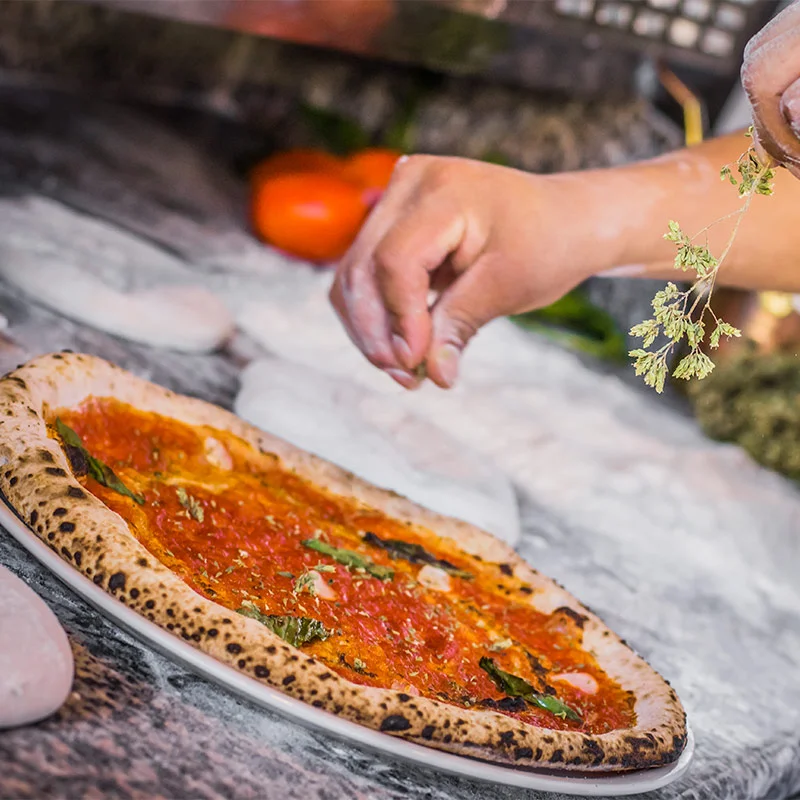 person garnishes pizza with fresh herbs