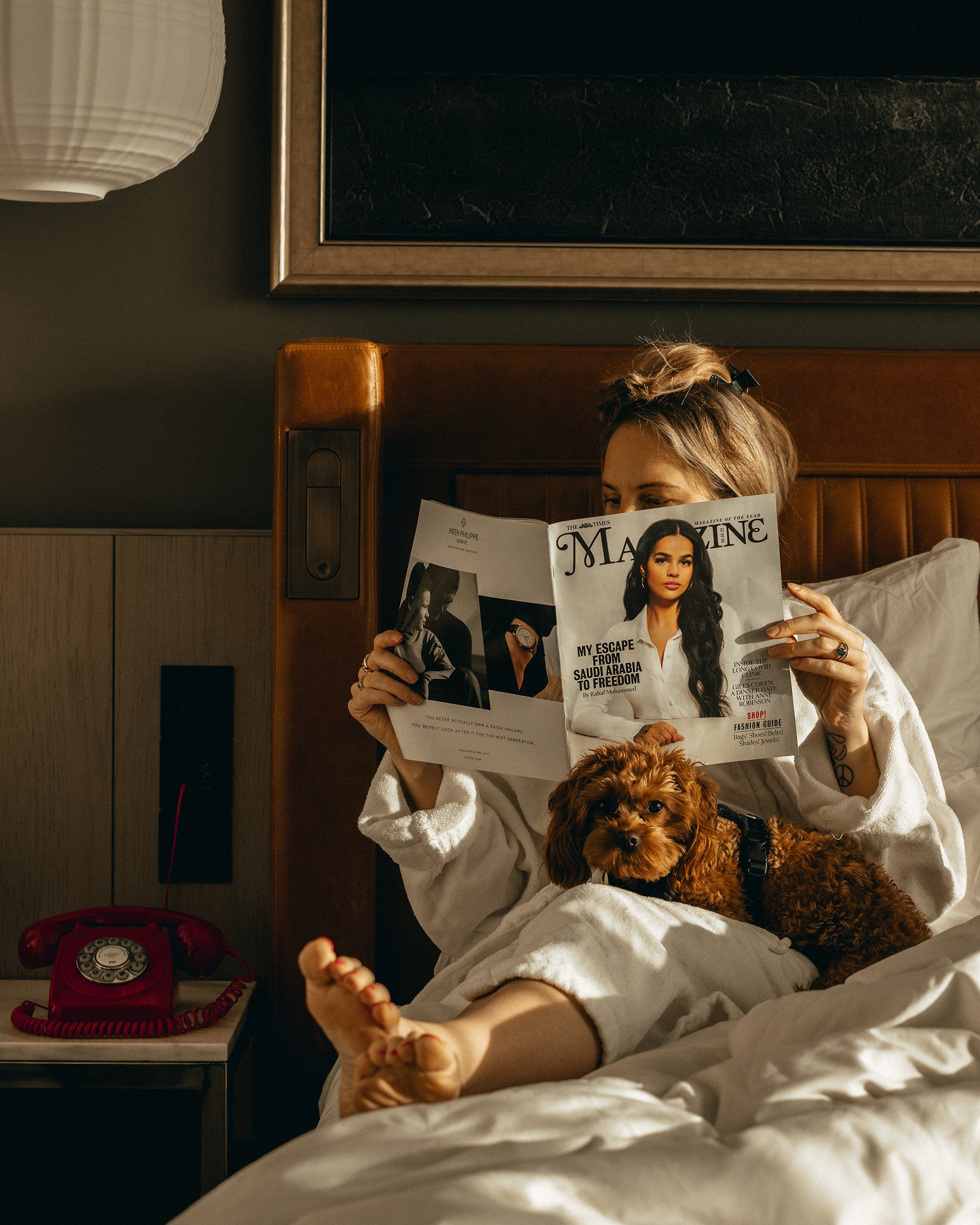 Girl in bed reading the paper with her dog on her lap