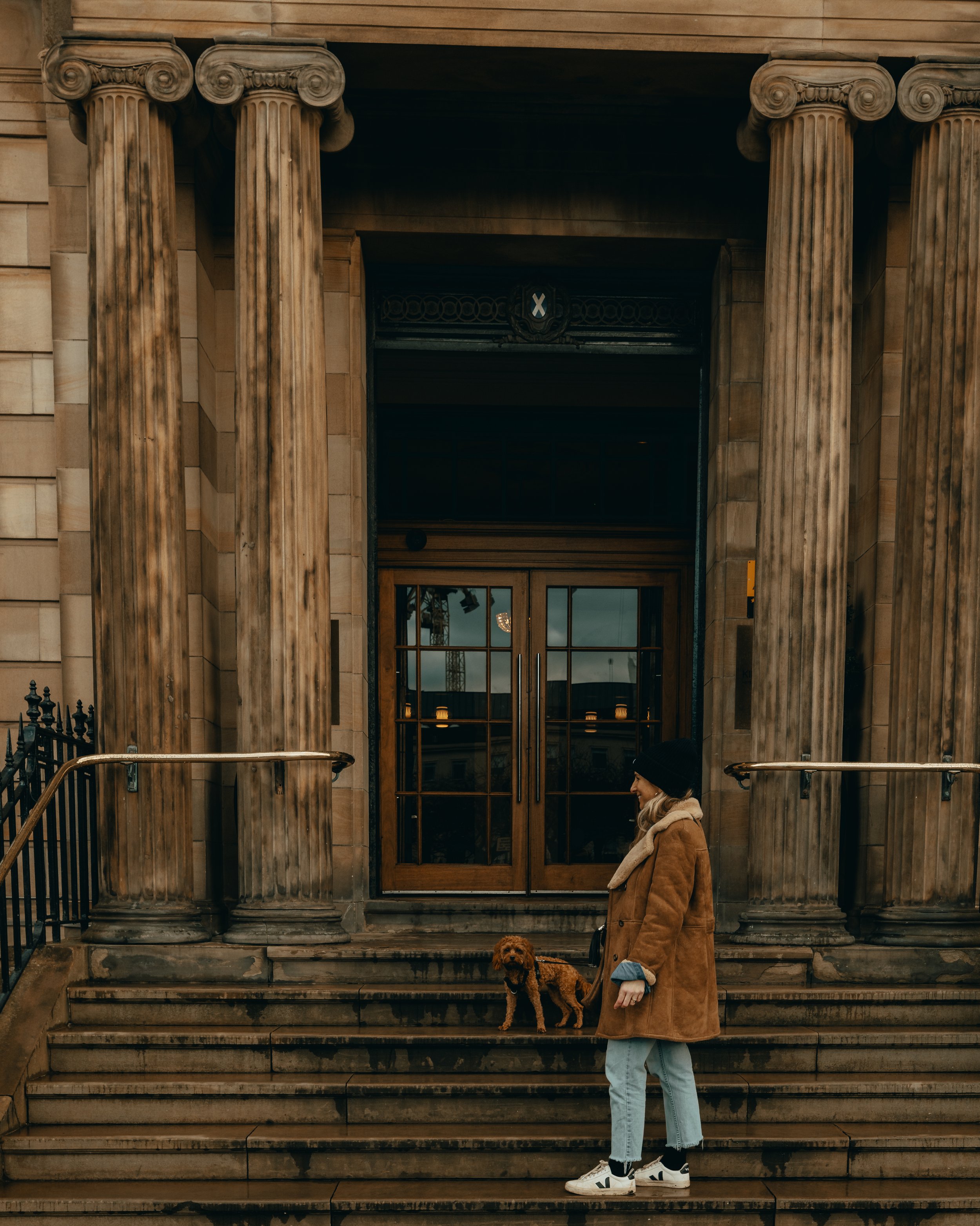 Girl with cavapoo dog stands on steps outside the hotel