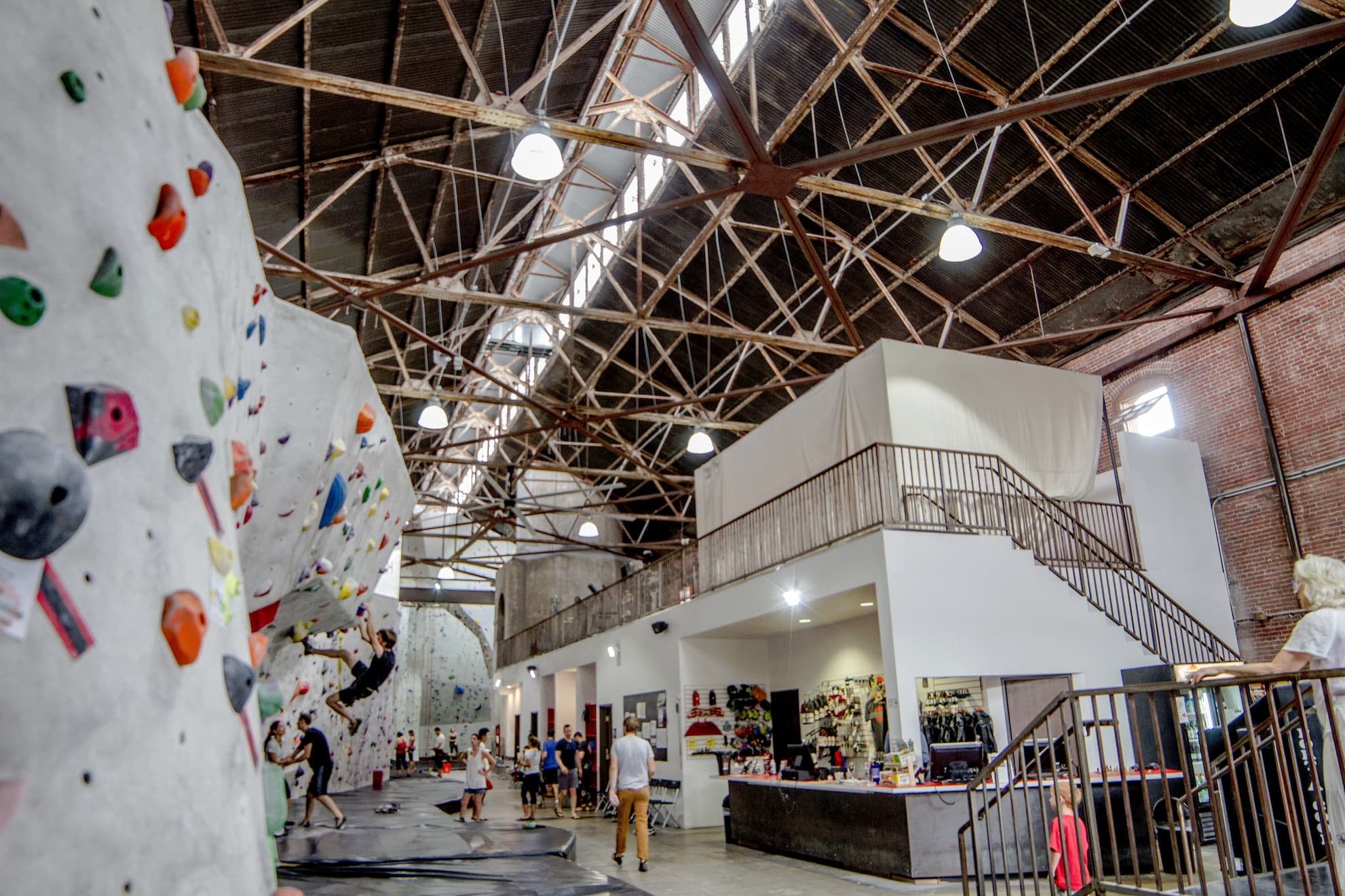 Indoor rock climbing gym with climbing wall and people climbing, socializing, and using the counter area.