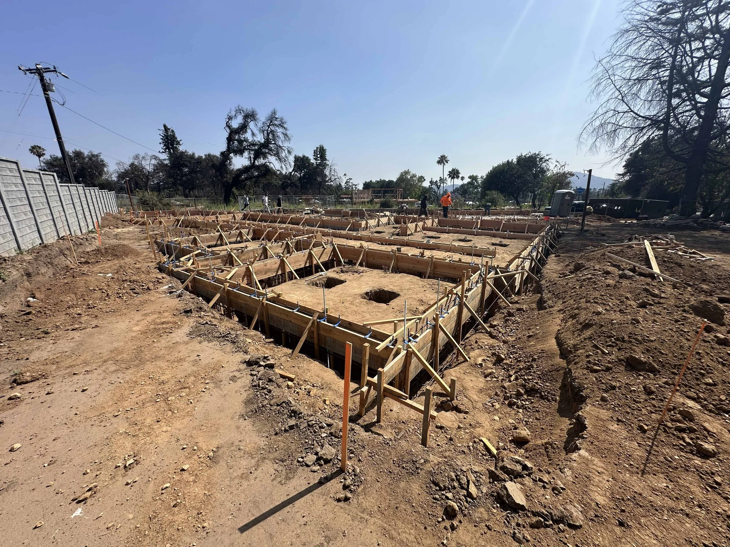 Construction site with wooden frames and workers in a clear outdoor area under a blue sky.